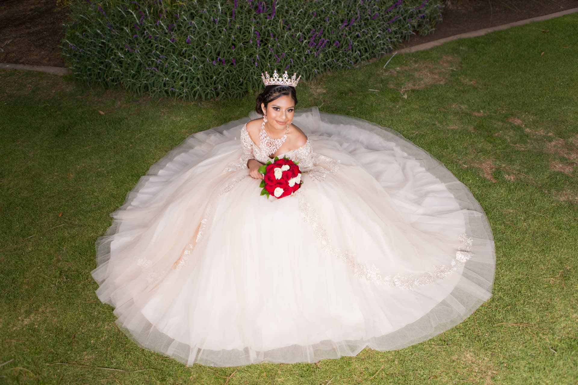 Quinceañera in a cream gown with her skirt spread in a circle on the grass at night holding a red and white bouquet