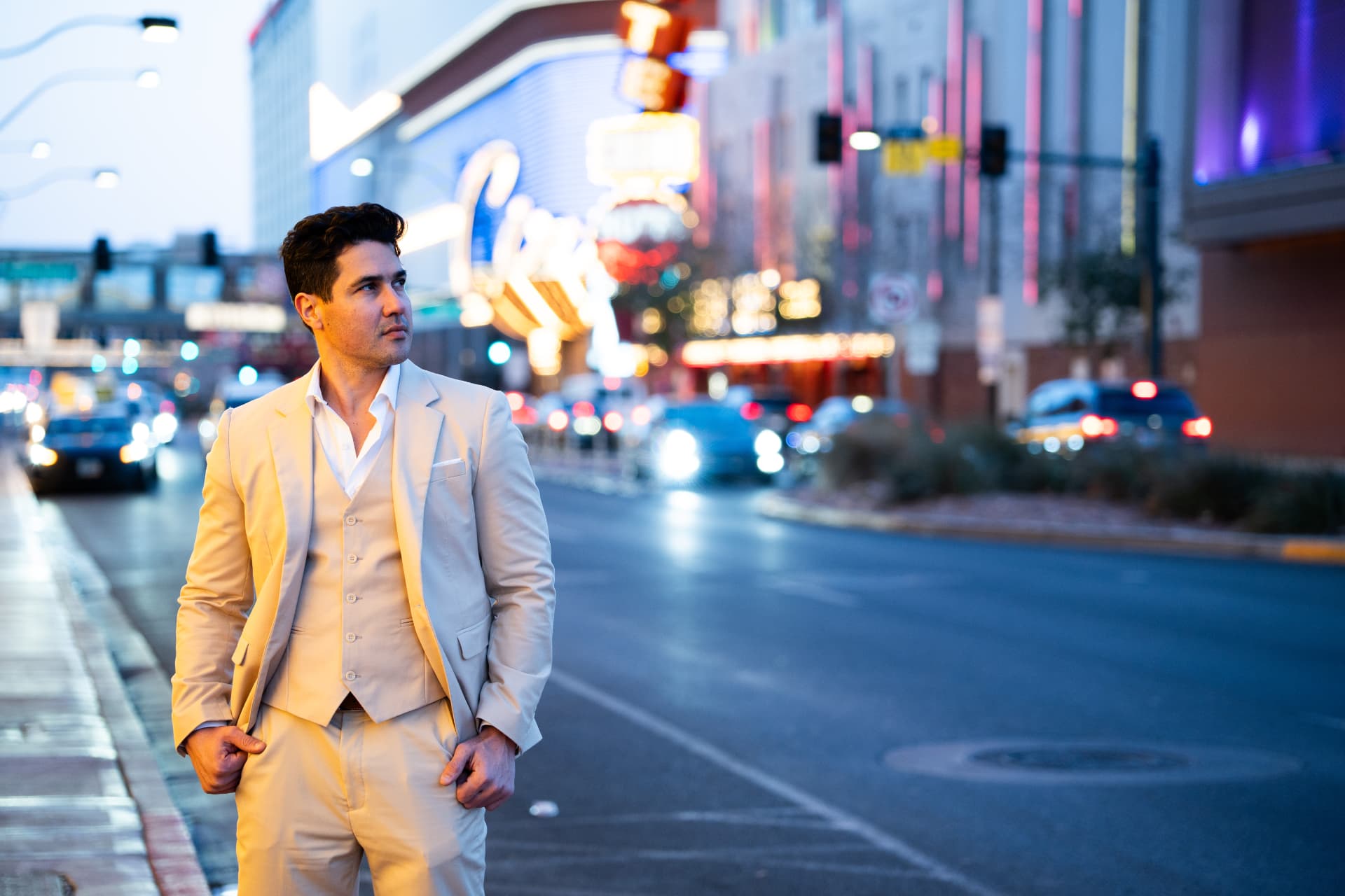 Groom in an ivory suit standing on a glowing city street at dusk
