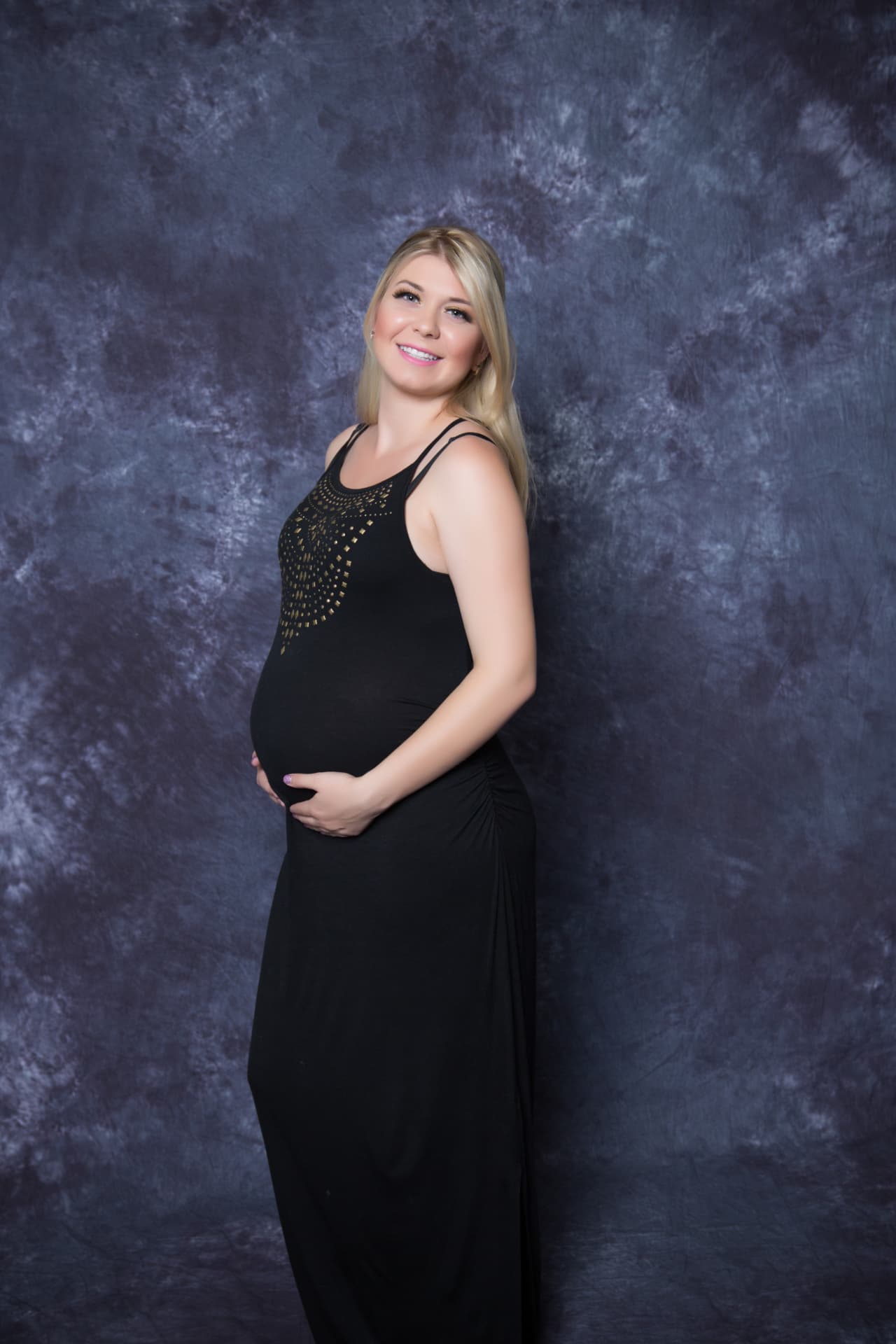 Expectant mother in a long black gown smiling in a studio portrait