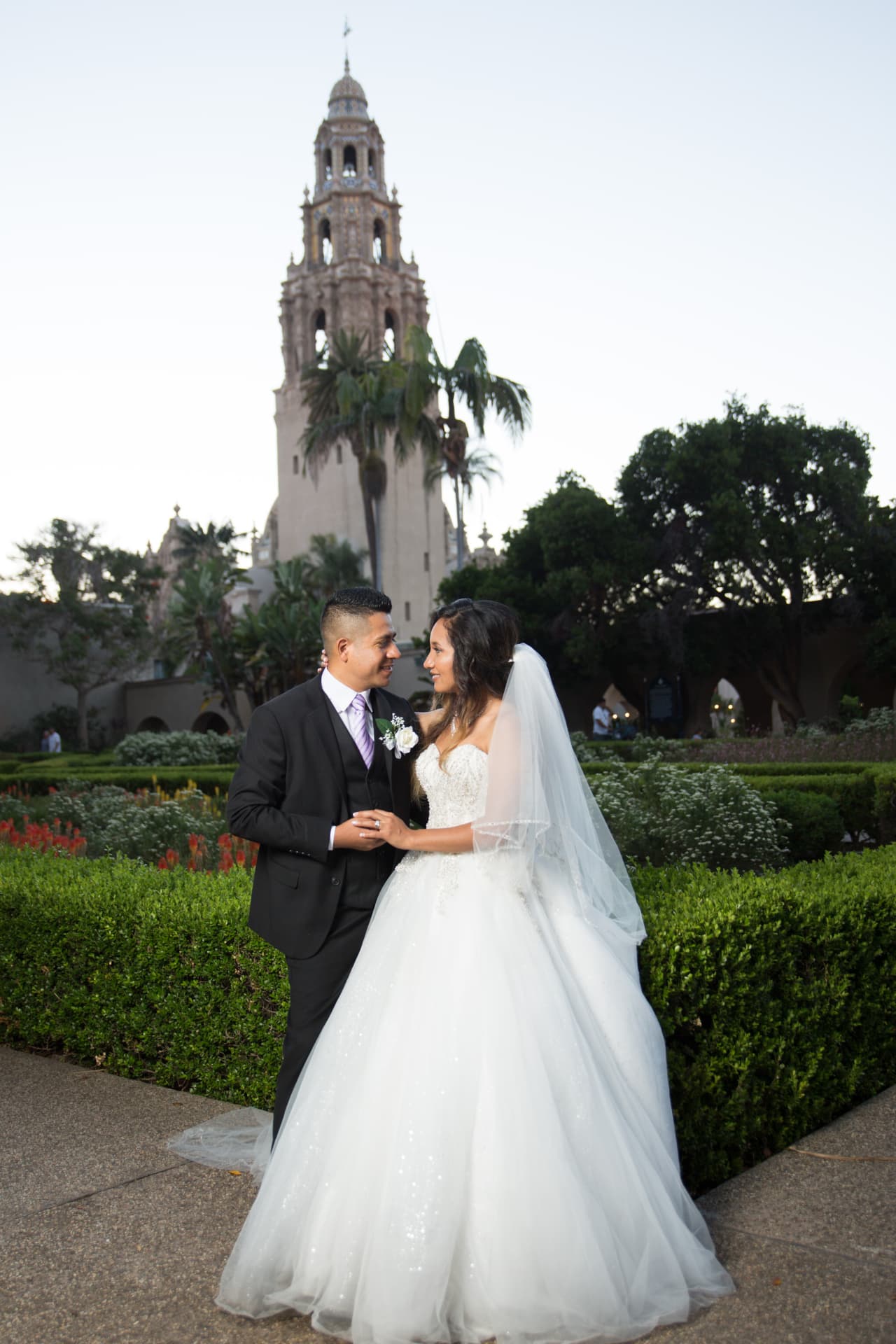 Bride and groom holding hands in a formal garden beneath a historic tower