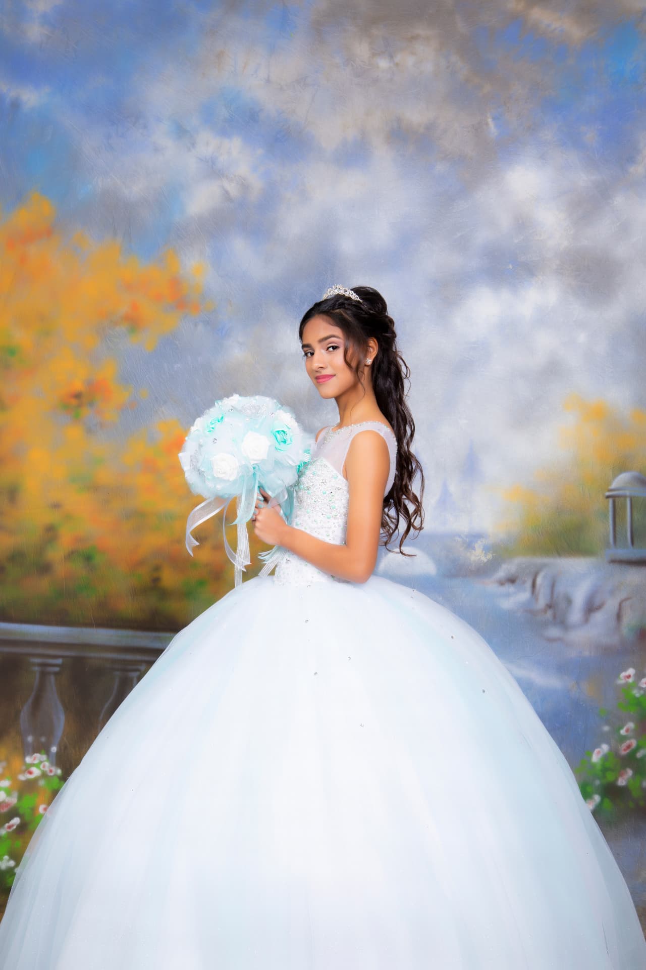 Quinceañera in a white gown holding a blue and white bouquet before a painted garden backdrop