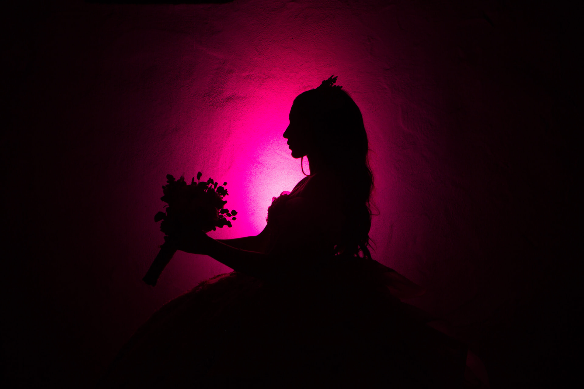 Quinceañera silhouette holding her bouquet against a glowing magenta-lit wall