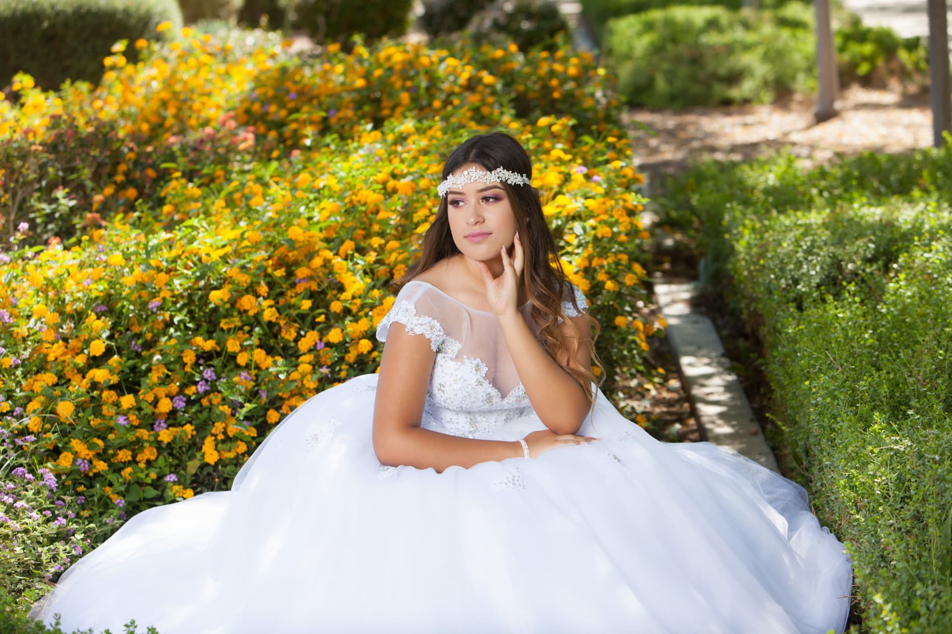 Quinceañera in a white gown resting her chin on her hand among yellow and orange flowers