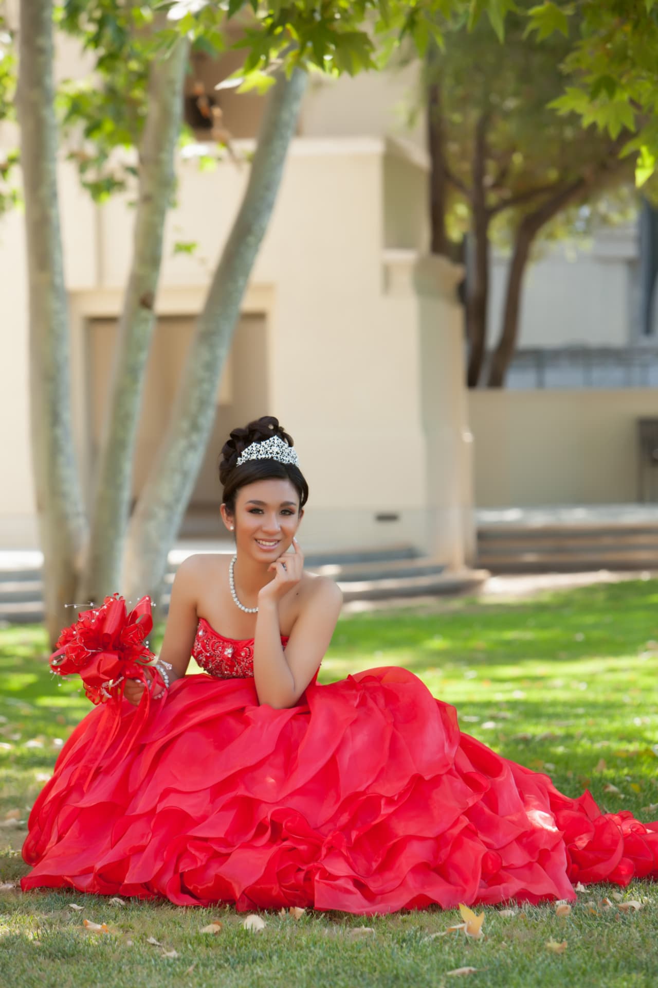 Quinceañera in a red and gold gown smiling by an old stone staircase at night