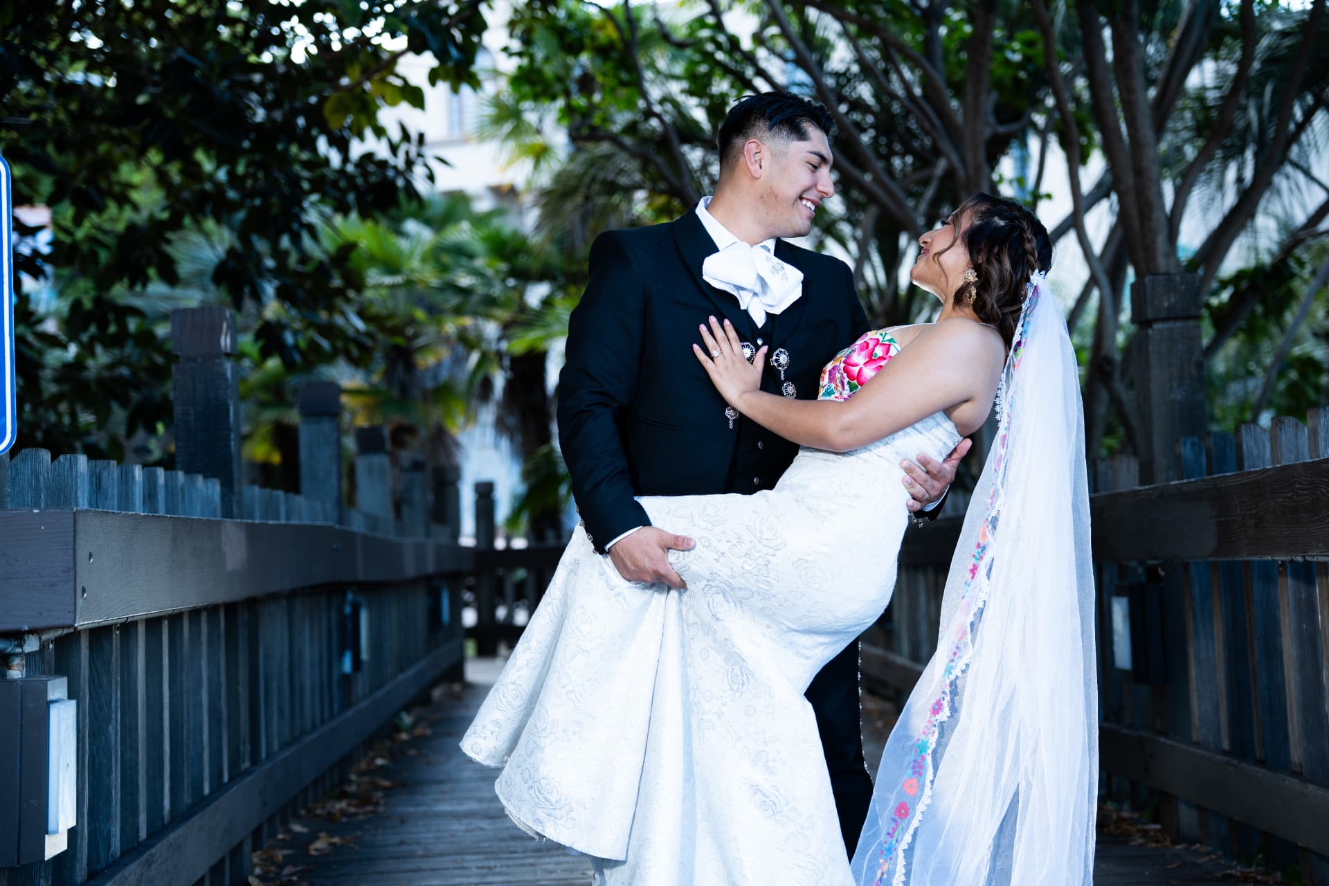 Groom in a charro suit holding his bride on a tree-lined boardwalk