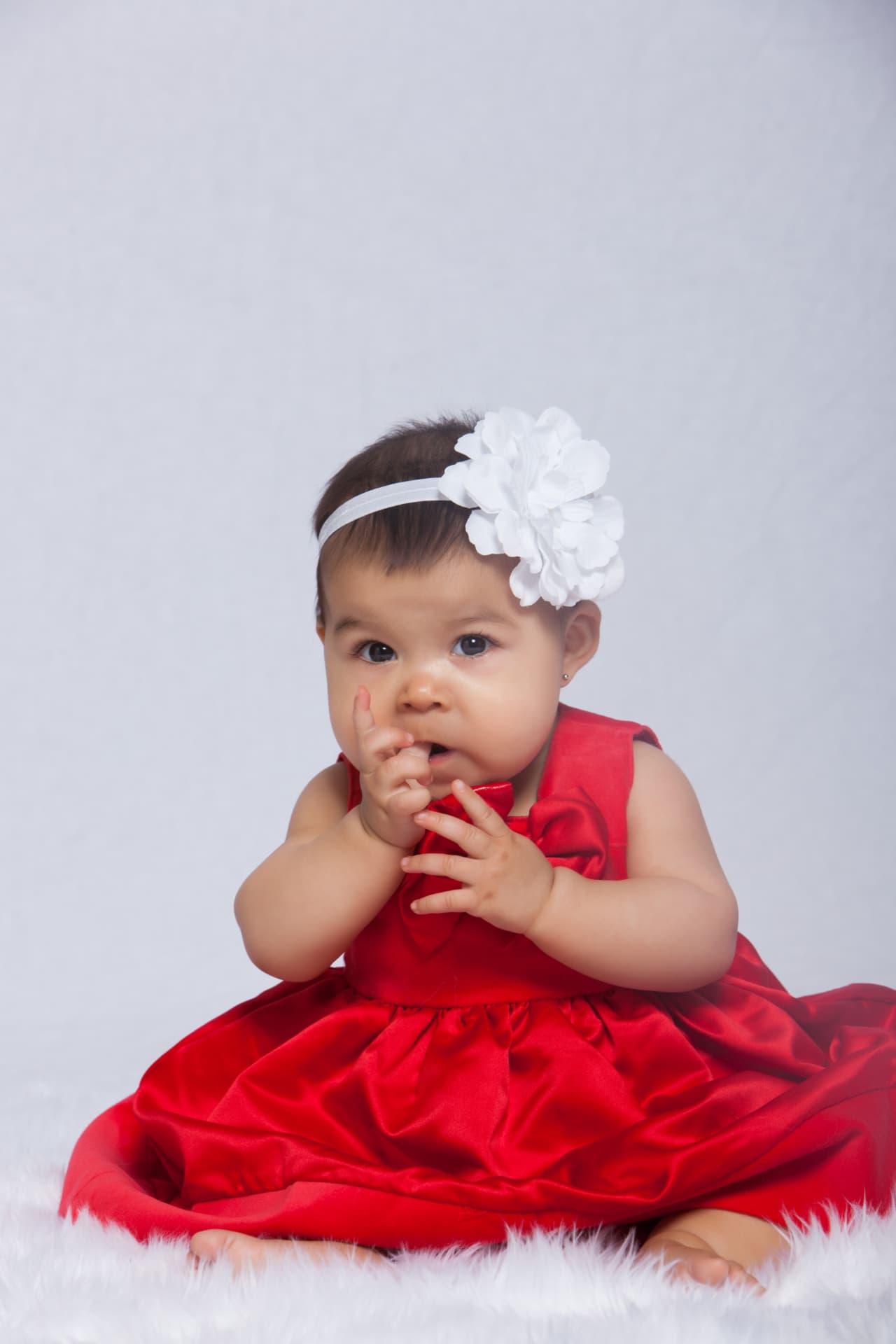 Baby girl seated in a red satin dress with a white floral headband