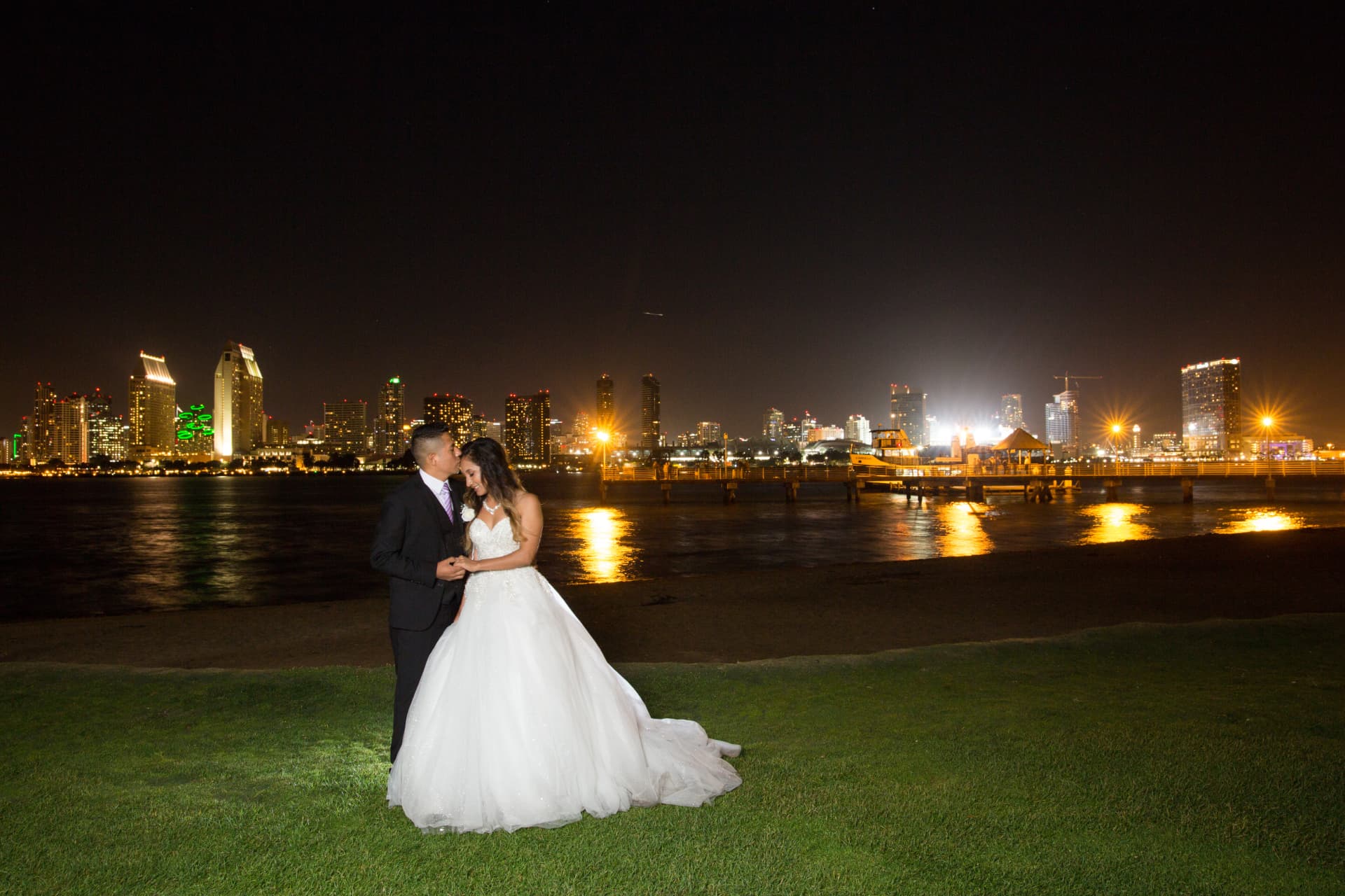 Bride and groom standing by the water with the city skyline glowing at night
