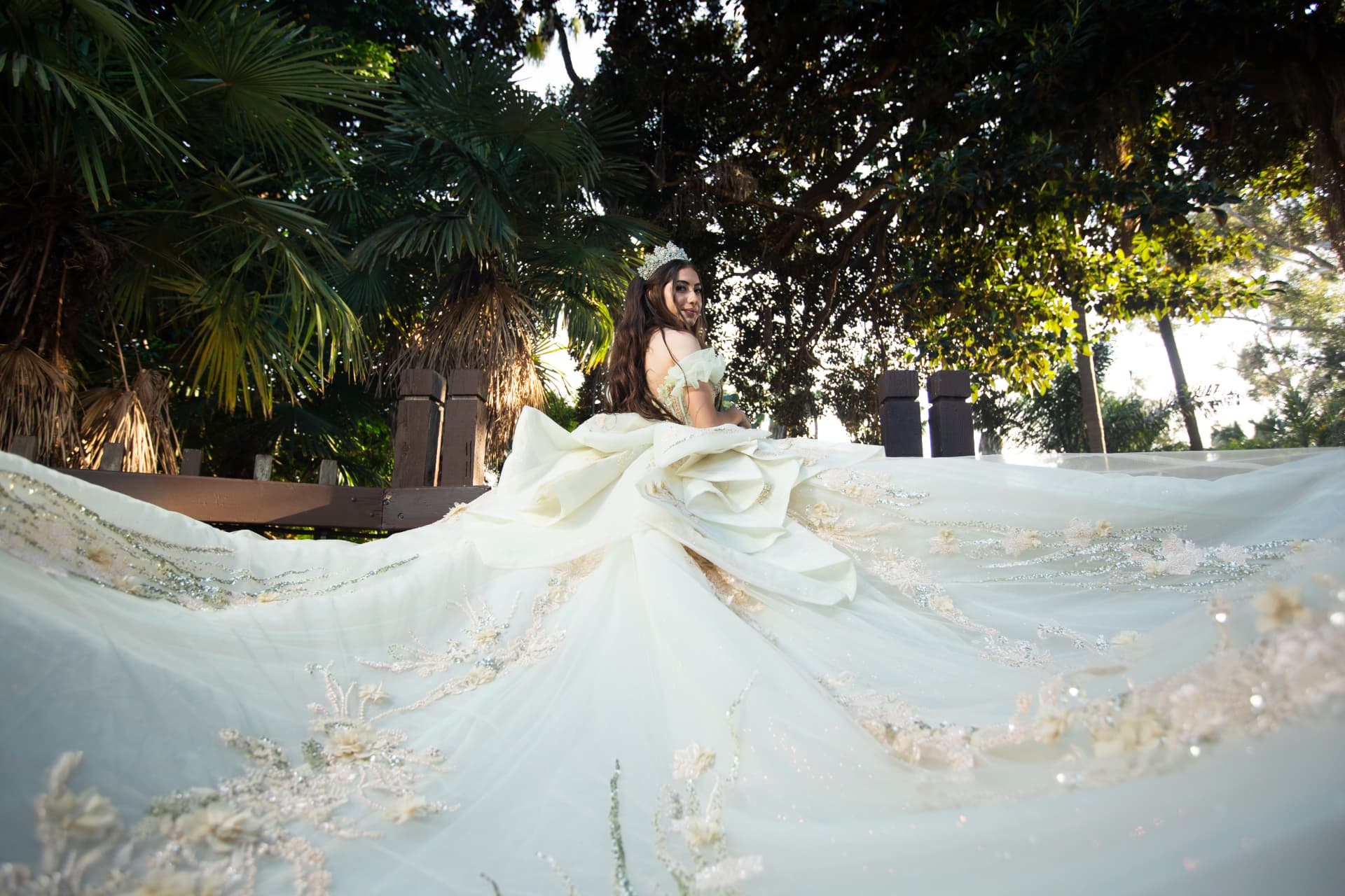 Quinceañera's sweeping gown train spreading across the ground among palm trees