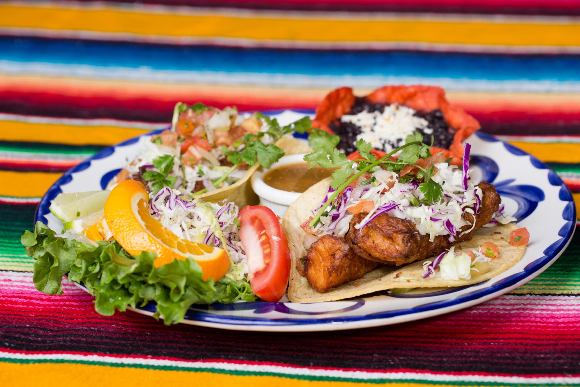 Crispy fish tacos topped with cabbage and pico de gallo on a colorful Mexican plate