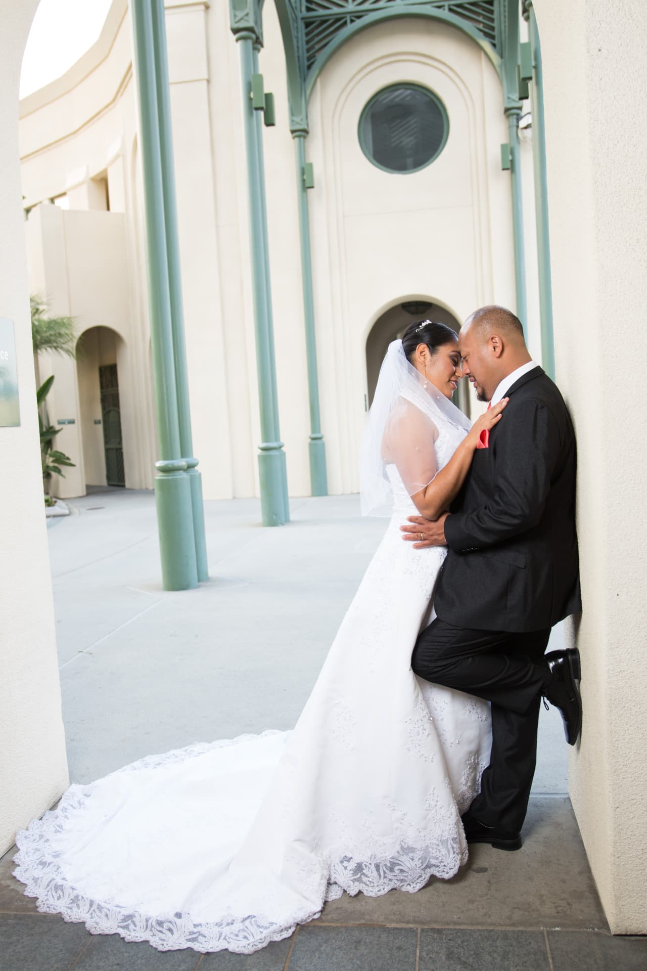 Bride and groom sharing an intimate moment beneath elegant green columns