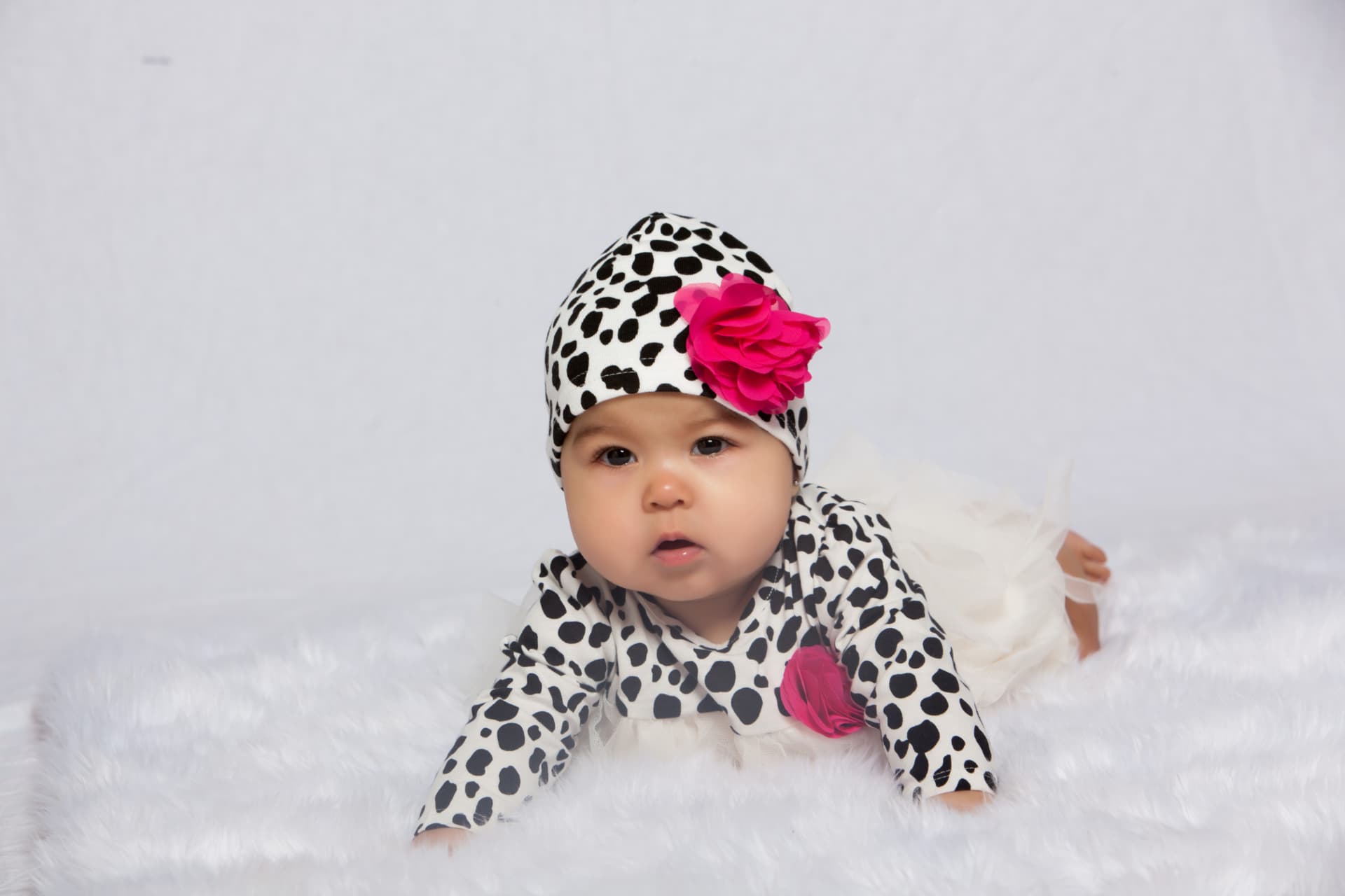Baby girl looking toward the camera in a spotted outfit with a bright pink flower
