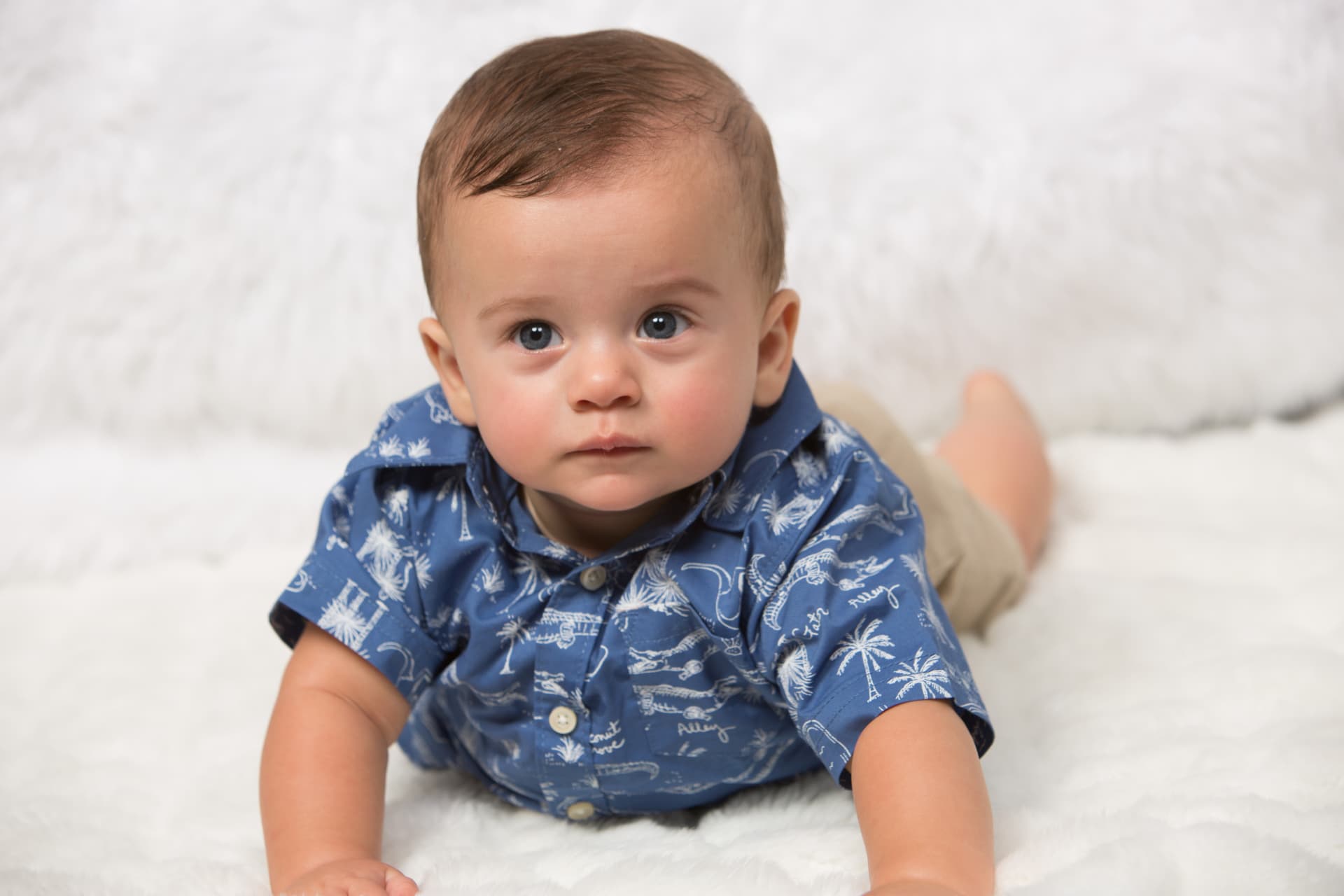 Baby boy in a blue patterned shirt lying on a soft white blanket