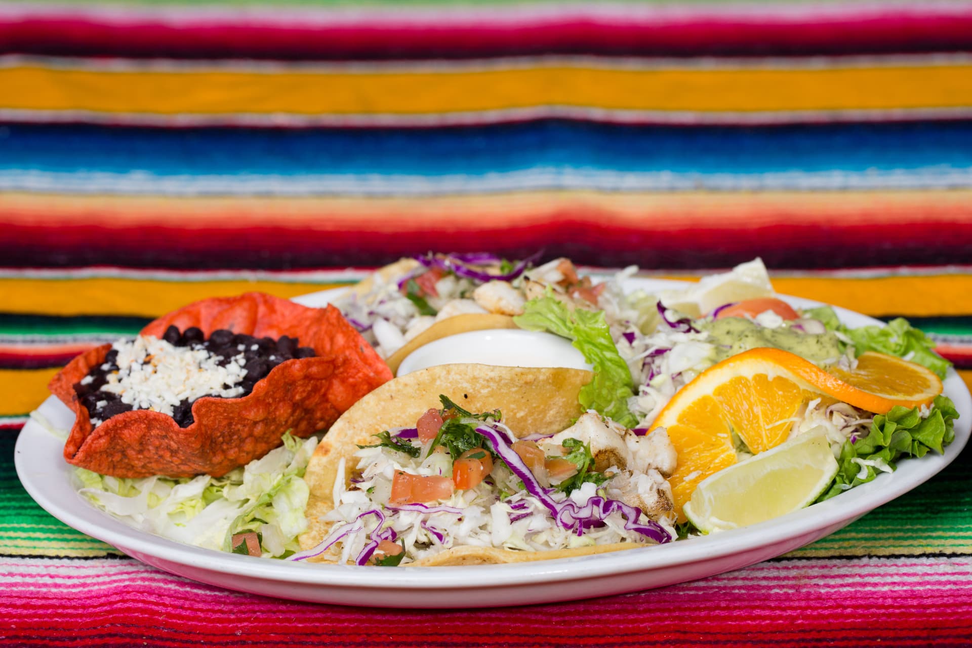 Fish taco combination plate with cabbage, pico de gallo, beans, salad, and citrus