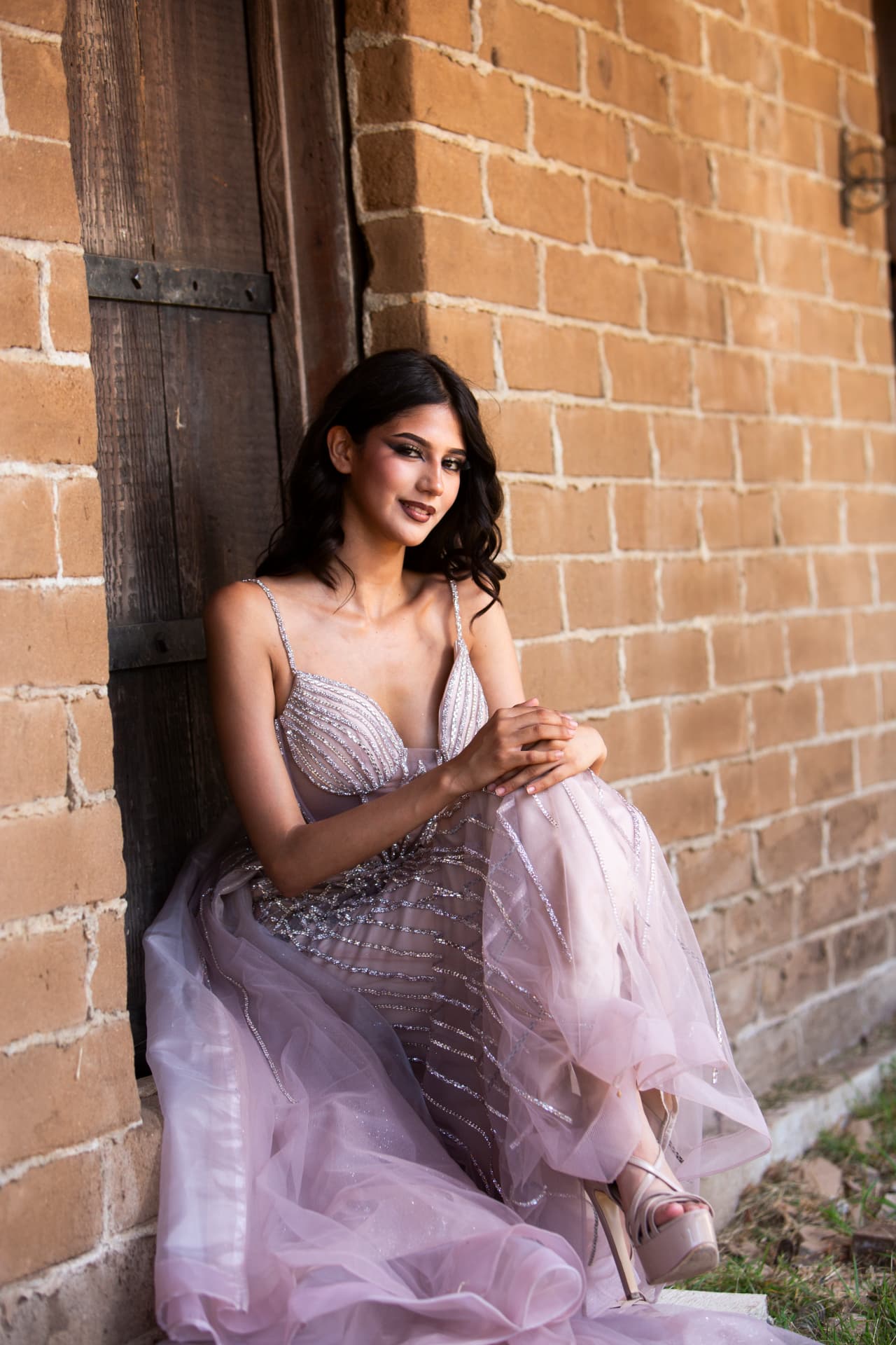 Model seated in a flowing blush gown beside a historic brick doorway