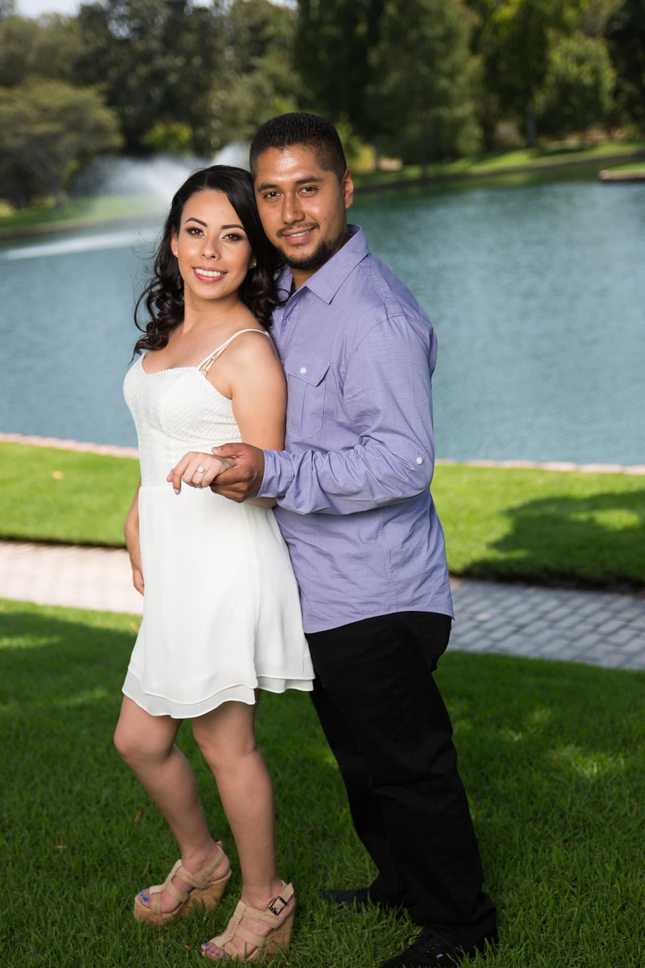 Engaged couple standing together on a lawn beside the lake