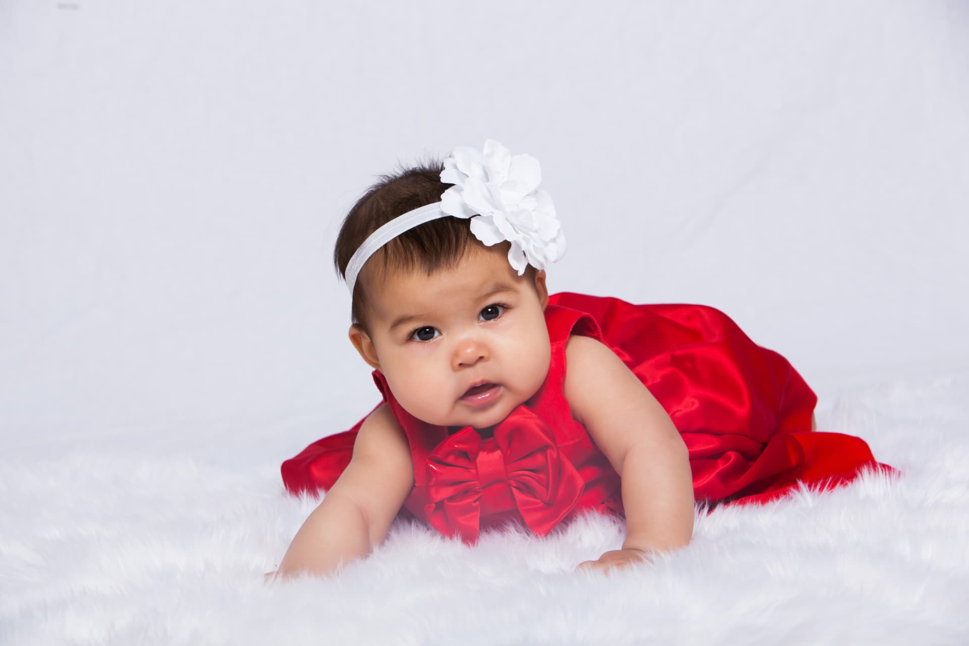 Baby girl looking toward the camera in a red satin dress