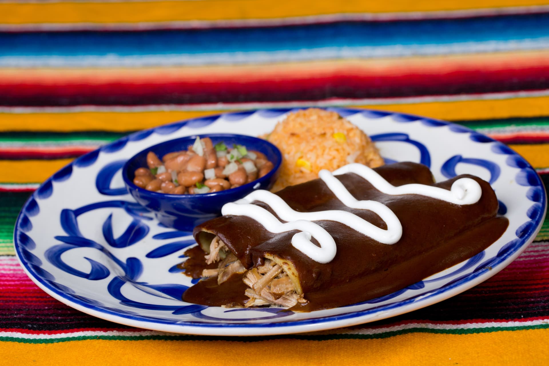 Chicken enchiladas in mole sauce finished with crema and served with rice and beans