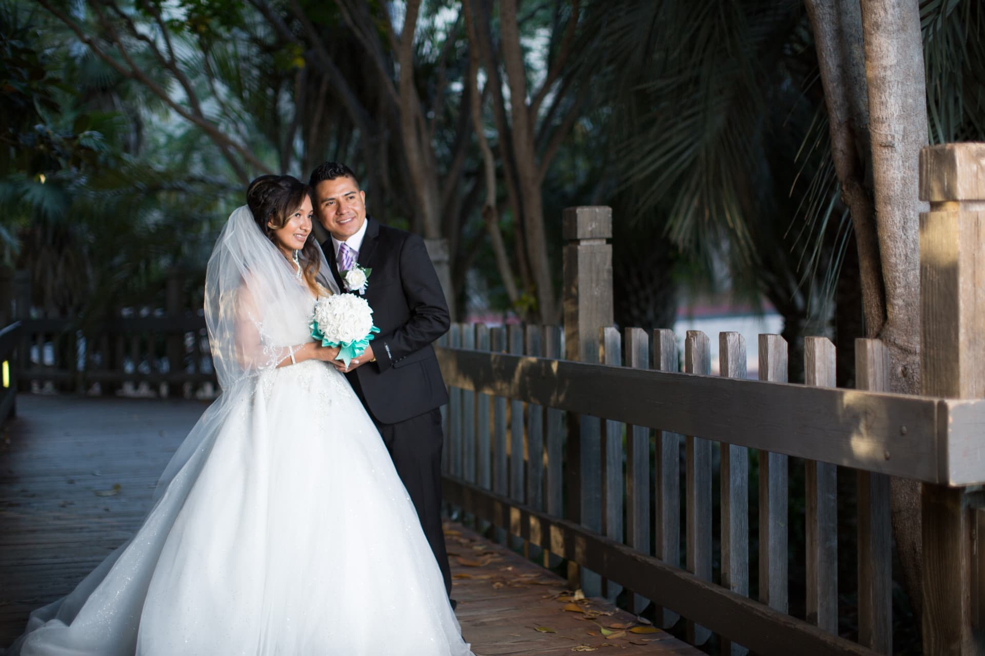 Bride and groom embracing beside a wooden fence in a tropical garden