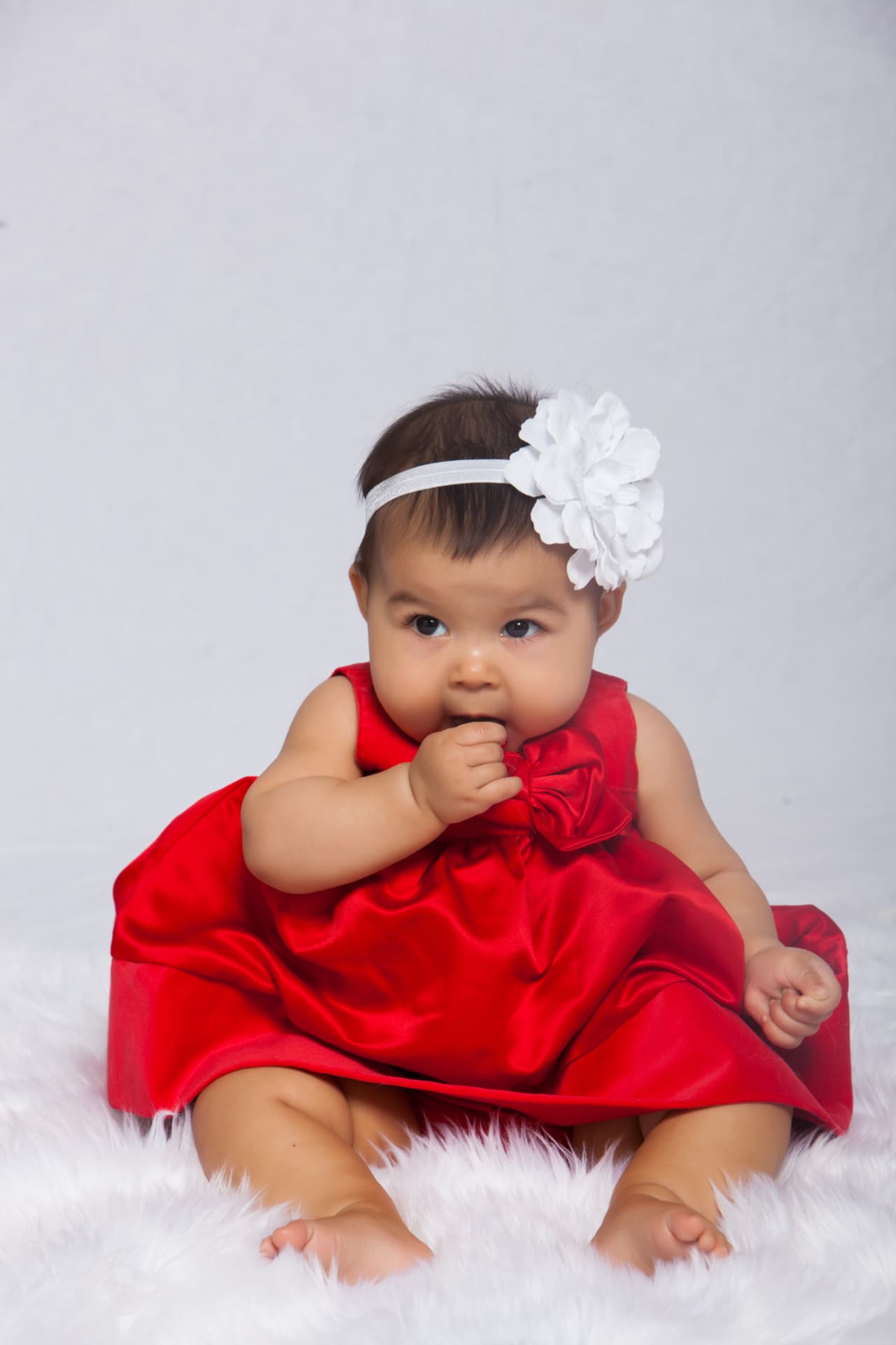 Baby girl seated in a red satin dress with a white flower headband