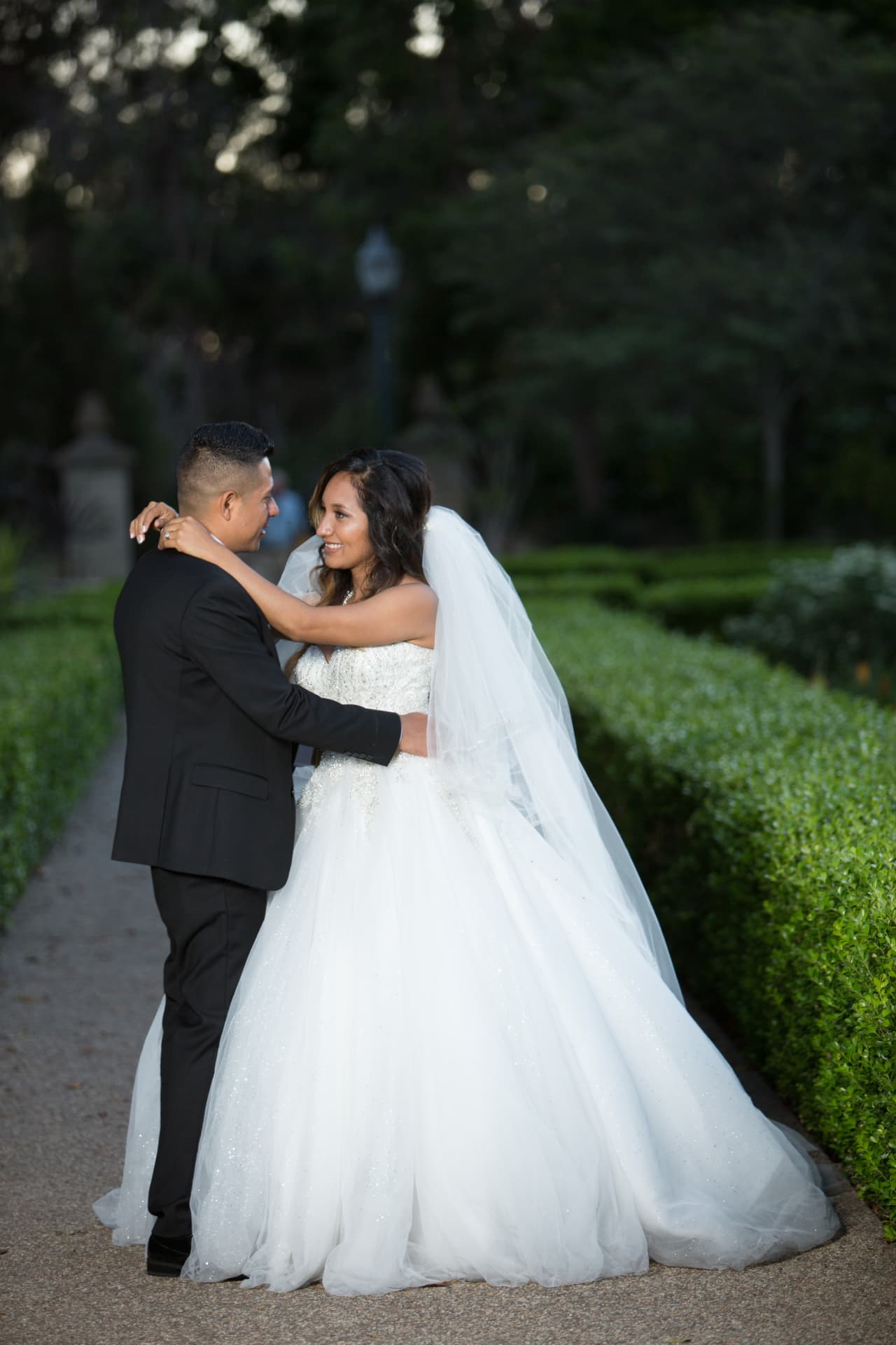 Bride and groom smiling at each other as they embrace on a garden path