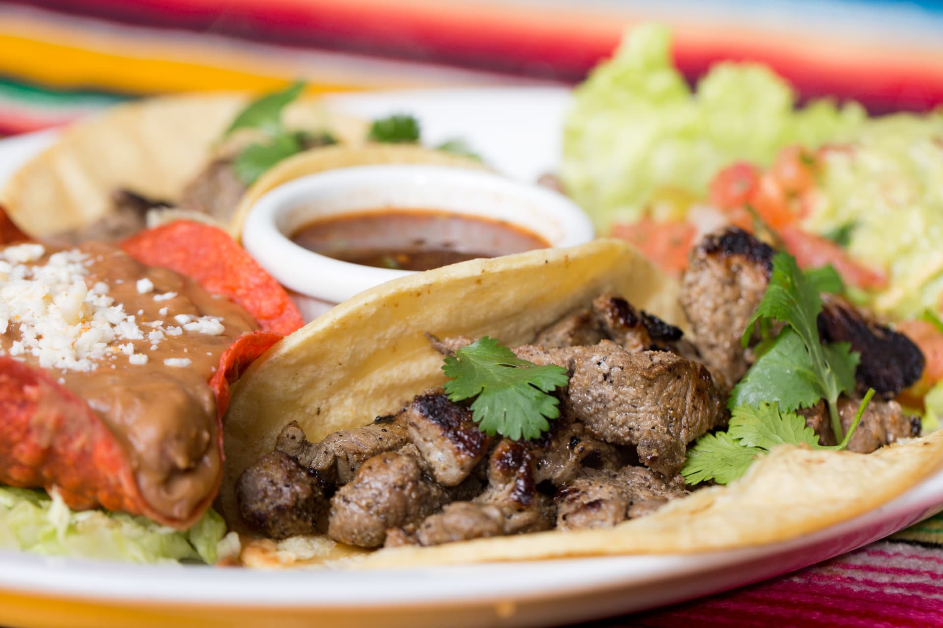 Carne asada tacos with cilantro served alongside beans, guacamole, and salsa