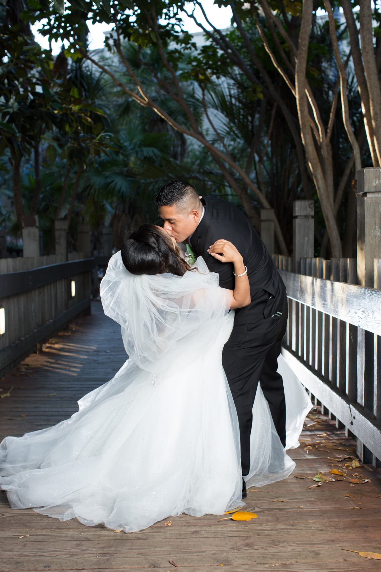 Groom dipping and kissing his bride on a shaded wooden boardwalk