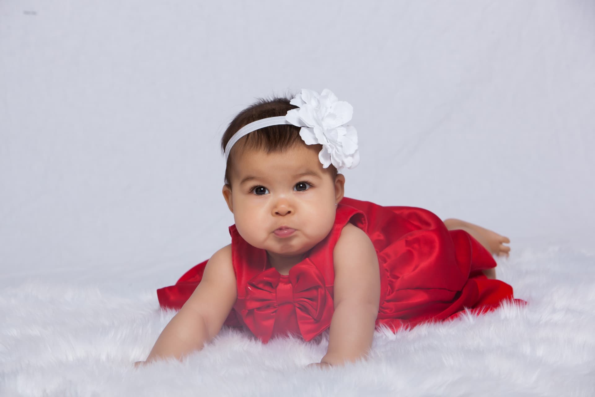 Baby girl crawling in a red satin dress and white floral headband