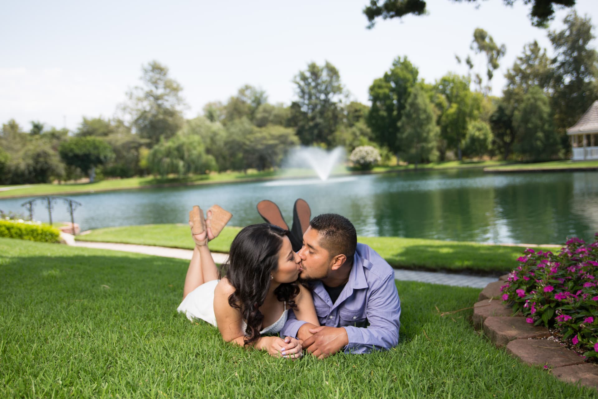 Engaged couple kissing while lying together on the grass beside a lake