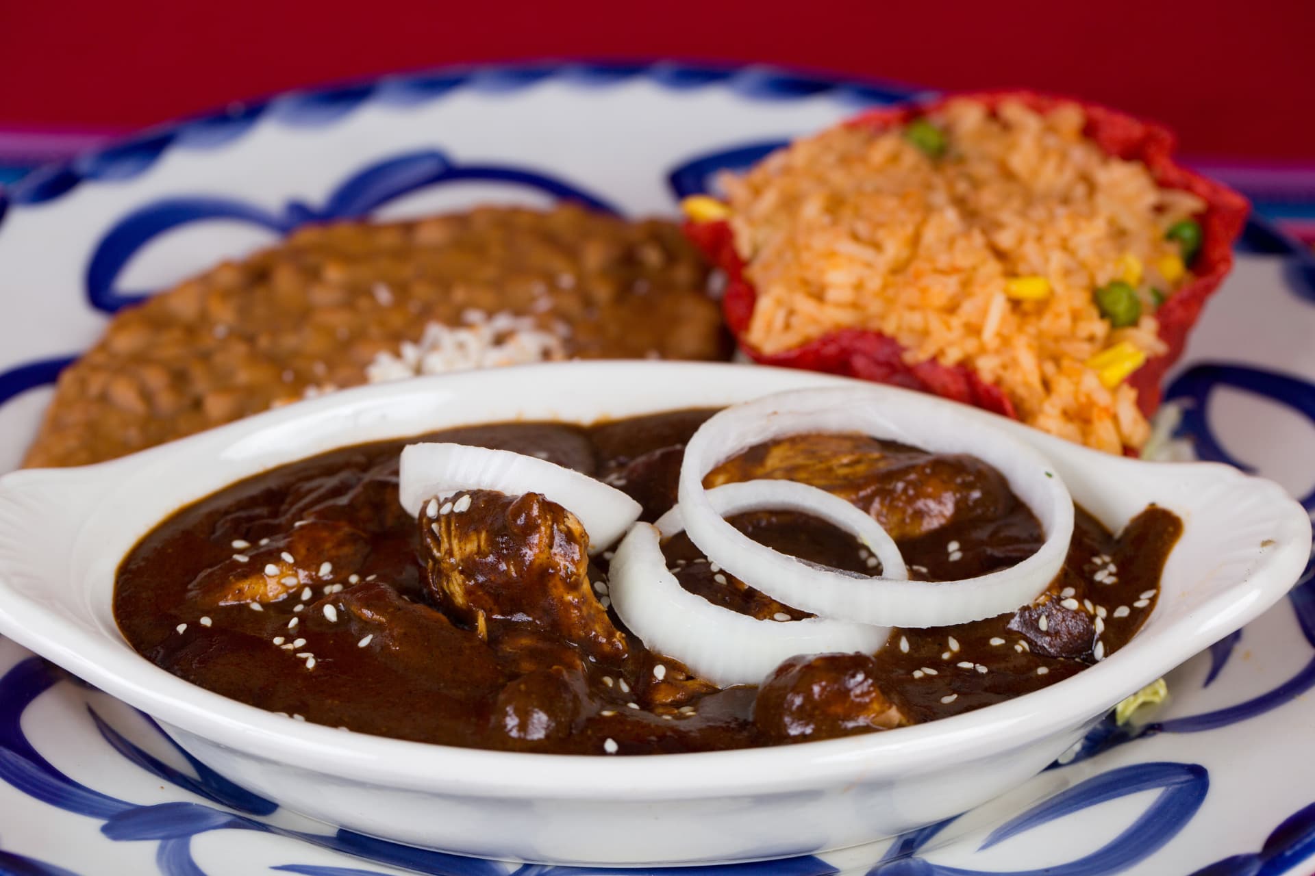 Chicken in rich mole sauce garnished with onion and sesame seeds with rice and beans