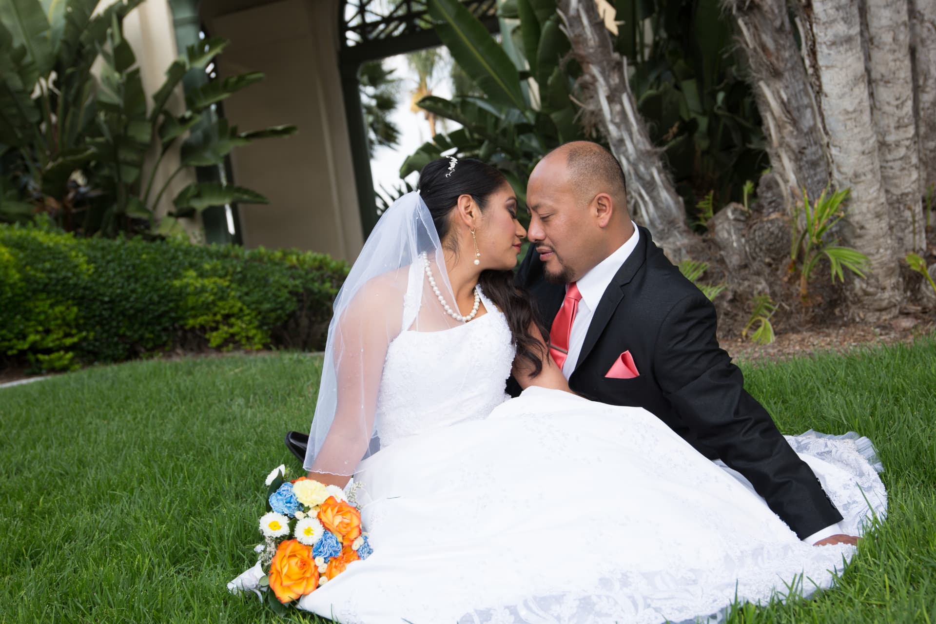 Bride and groom seated together on the grass with a colorful bouquet