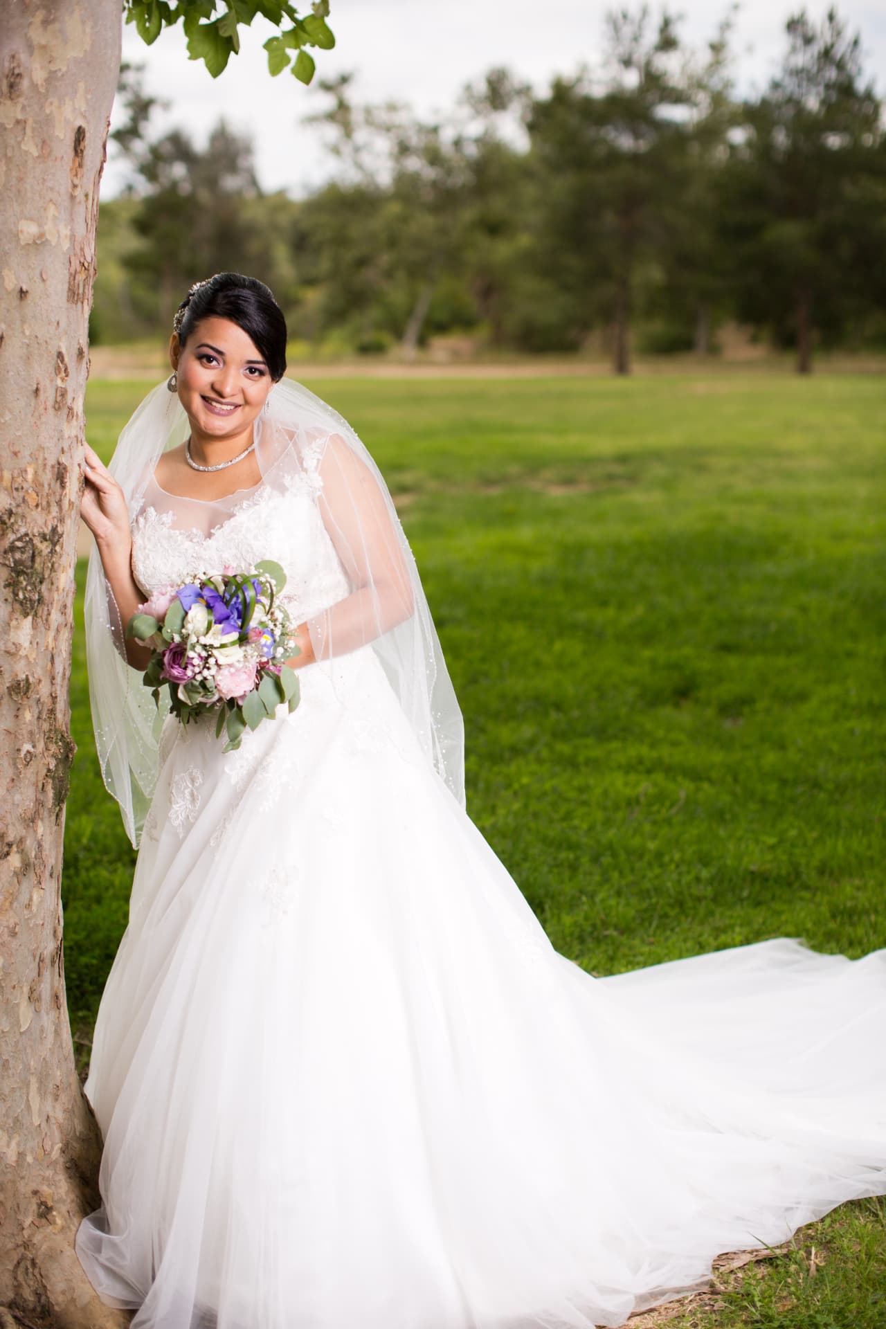 Smiling bride with a colorful bouquet posing beside a tree in a green park