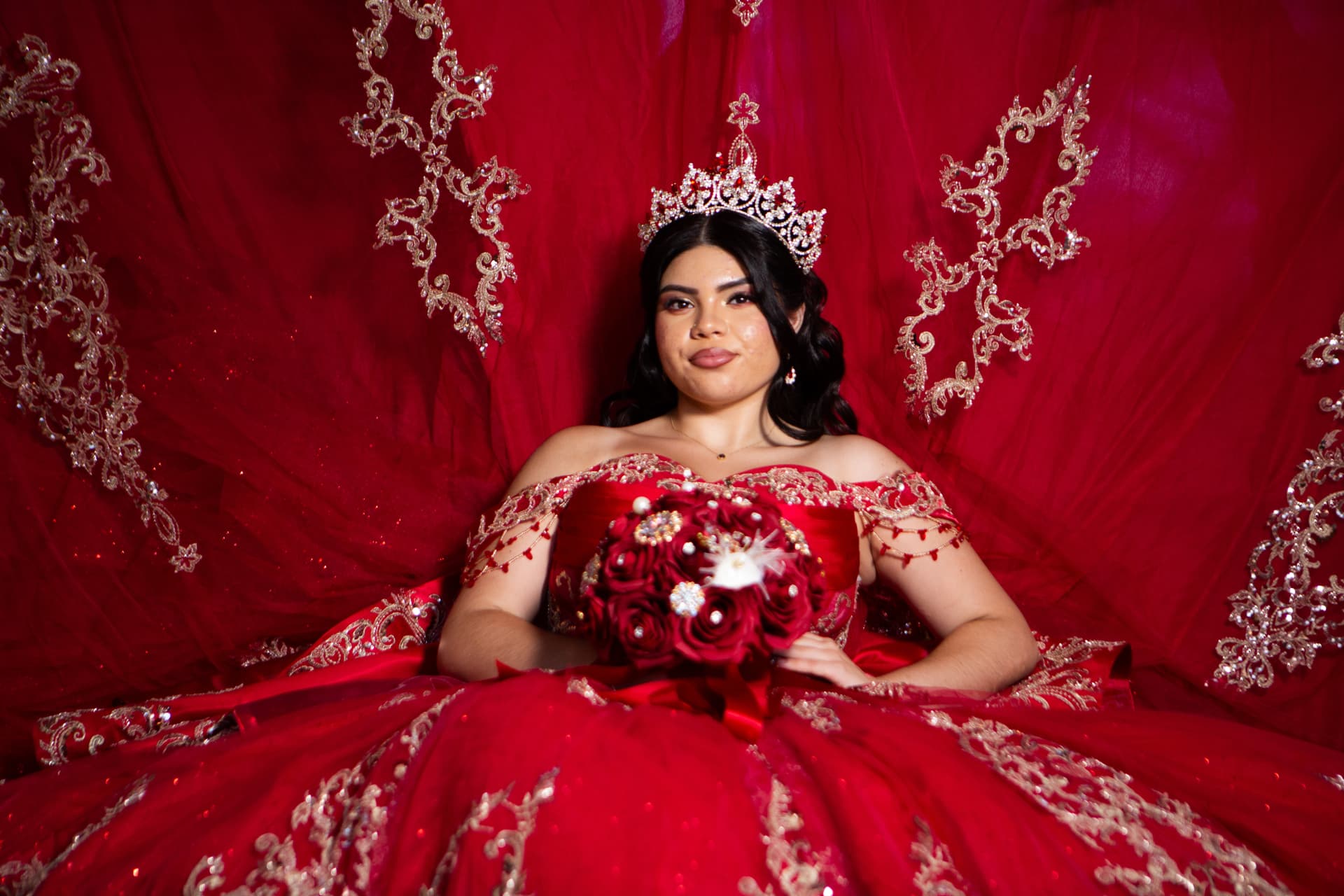 Quinceañera in a red gown holding her bouquet against a draped red backdrop