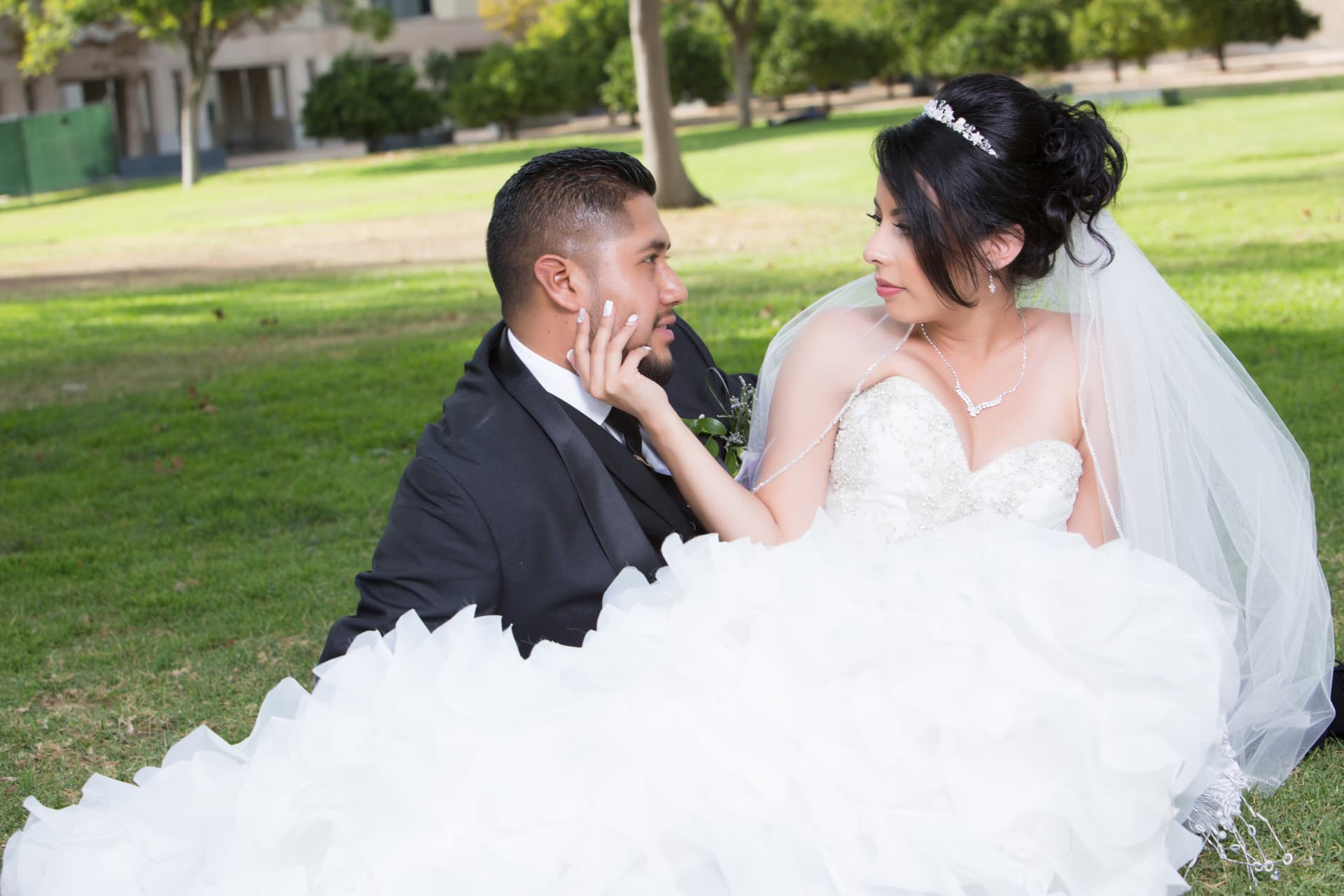 Bride and groom seated on the grass and looking into each other’s eyes