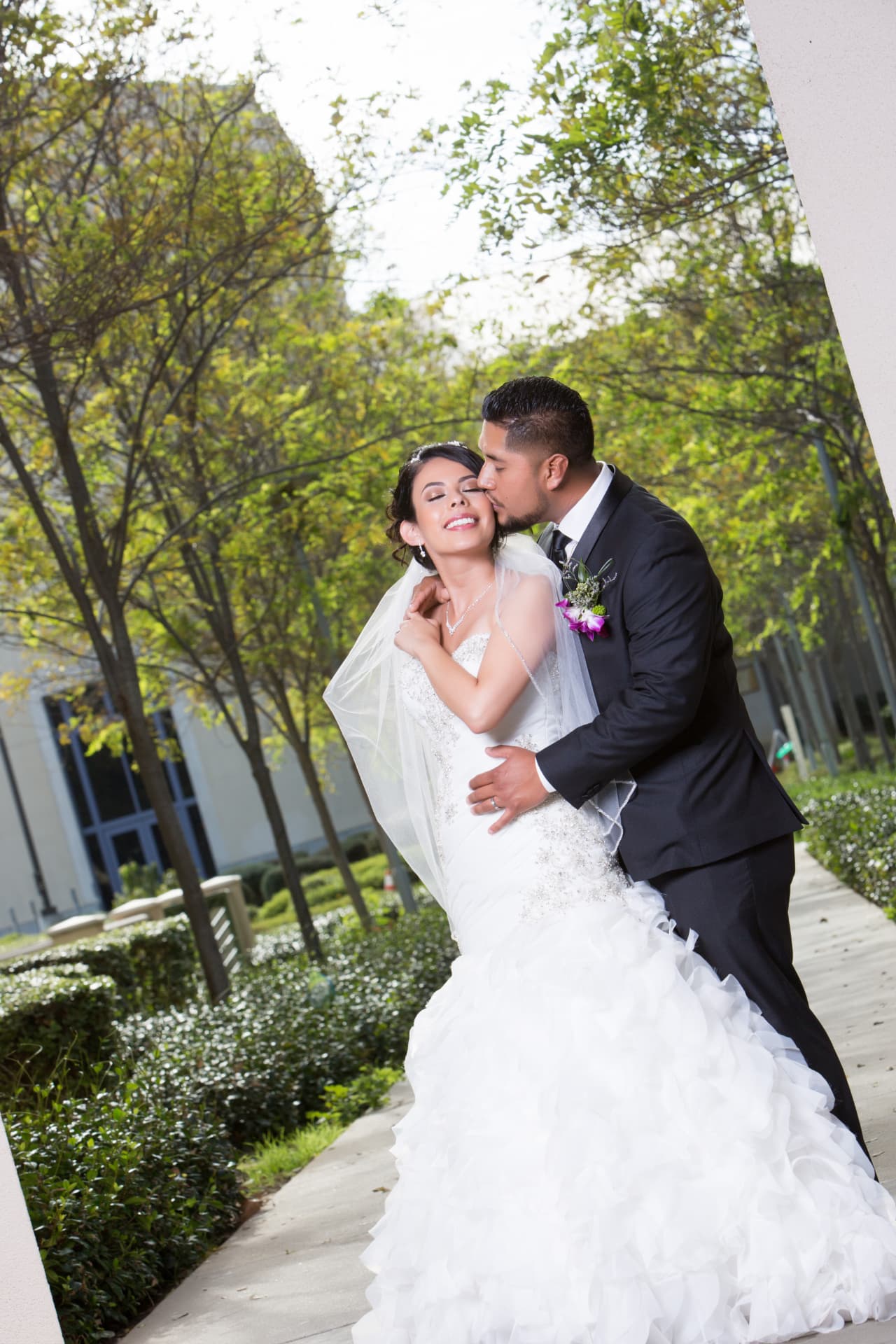 Groom embracing and kissing his smiling bride in a sunlit garden