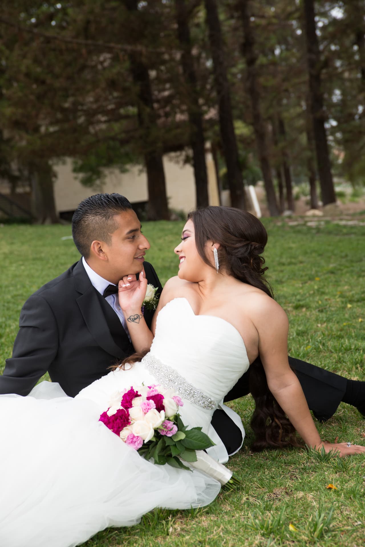 Bride and groom smiling at each other while seated together on the grass