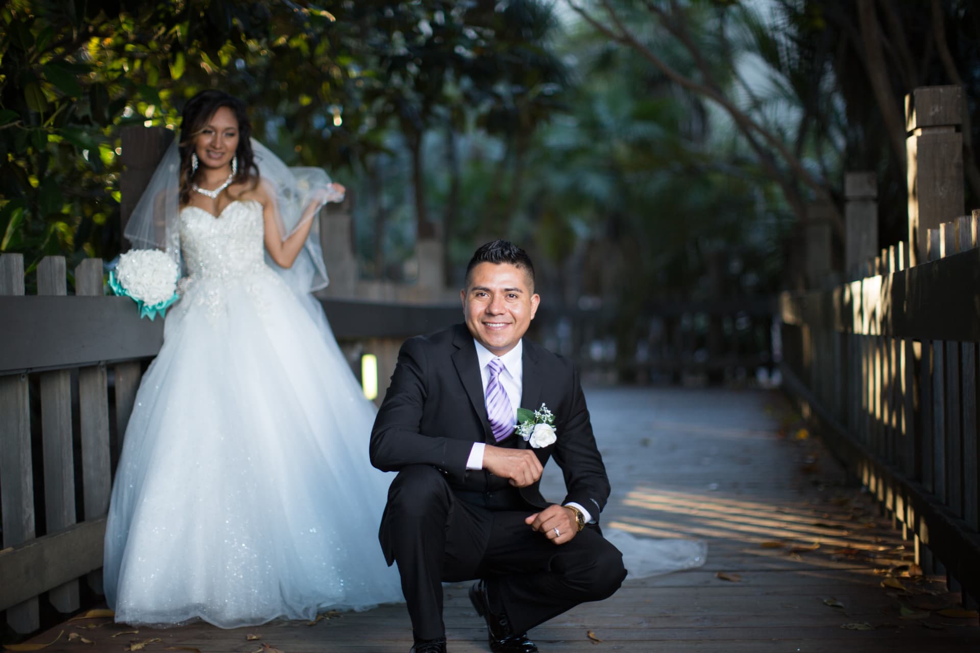 Bride standing behind her groom for a formal portrait on a shaded wooden boardwalk