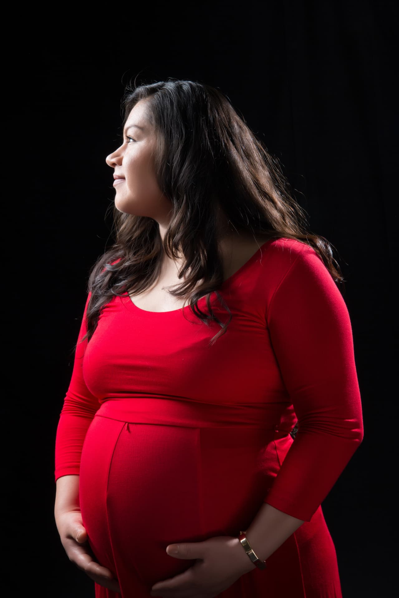 Expectant mother in a red gown illuminated against a black background