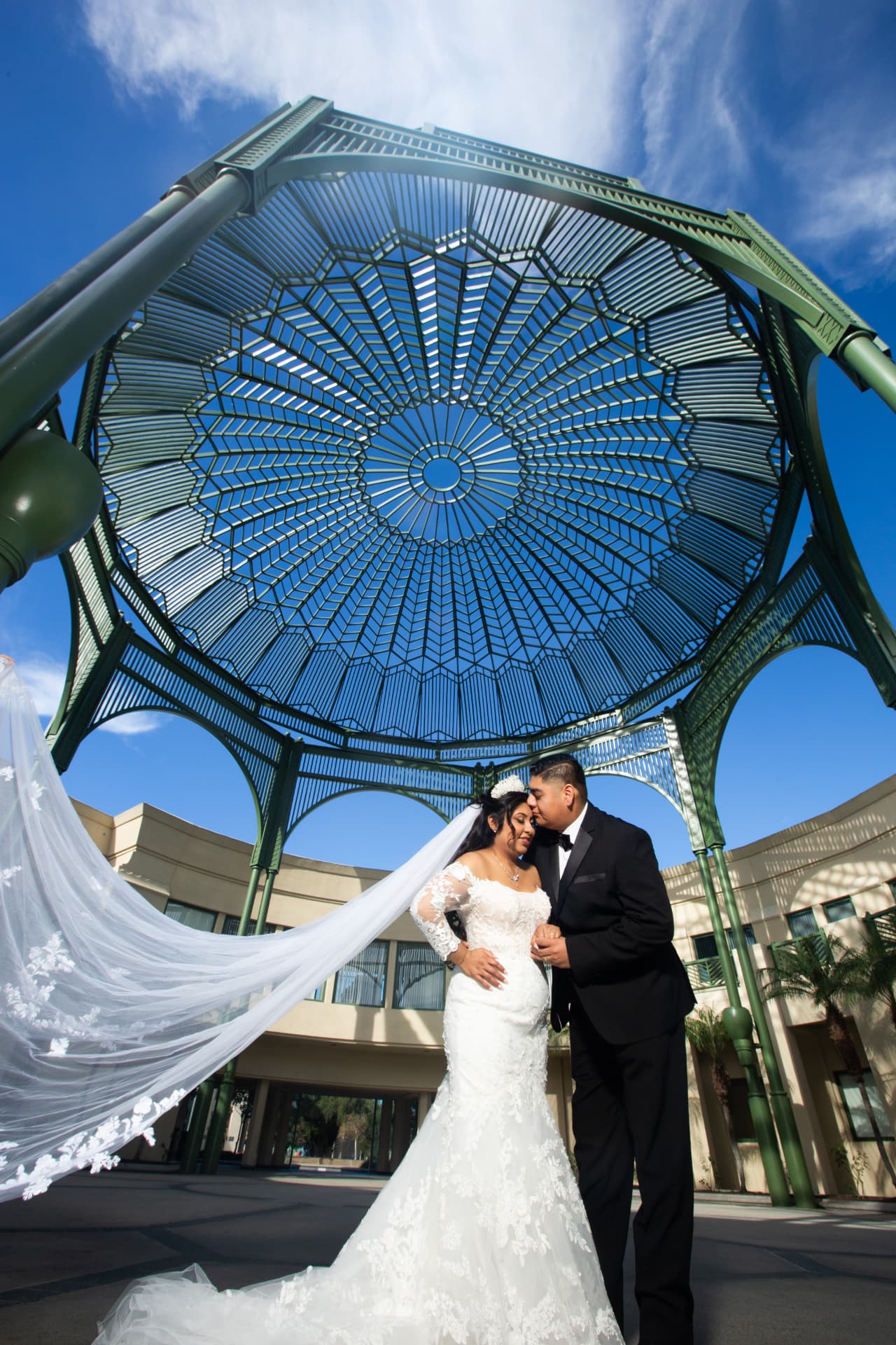 Bride and groom standing beneath an ornate open-air gazebo