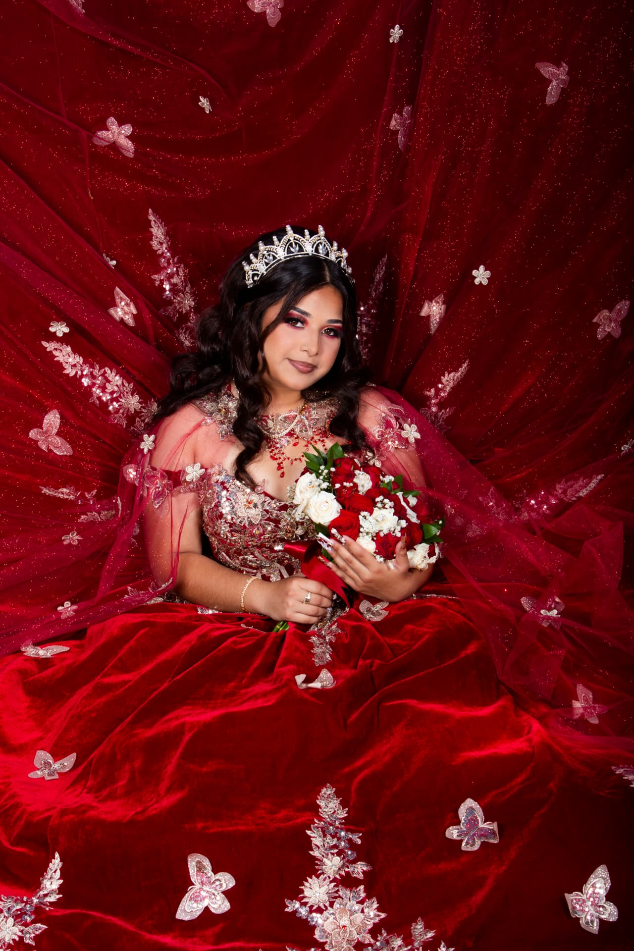 Quinceañera in a red velvet gown with her gown and veil spread wide around her