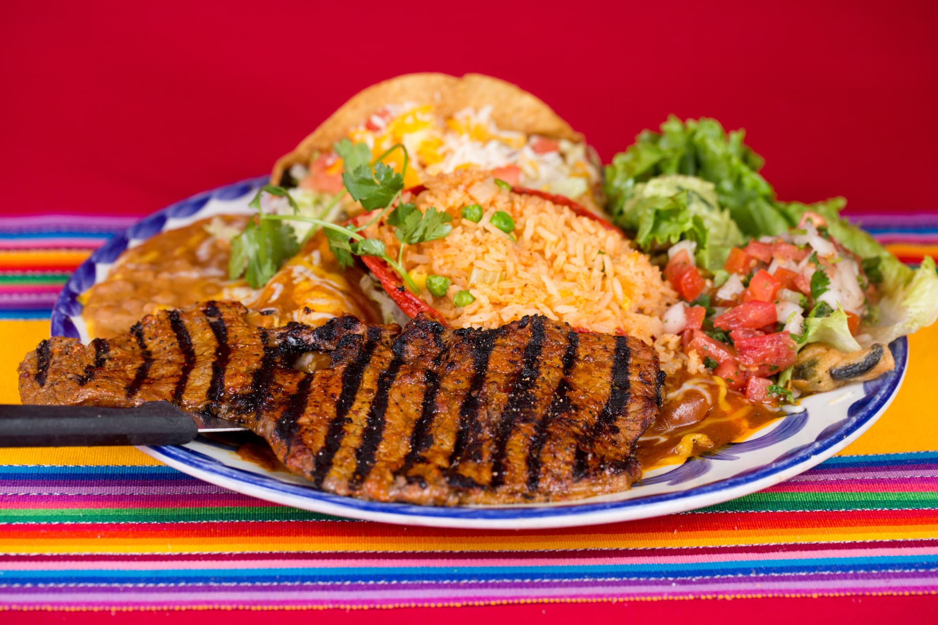 Grilled steak served with enchiladas, rice, beans, salad, and guacamole