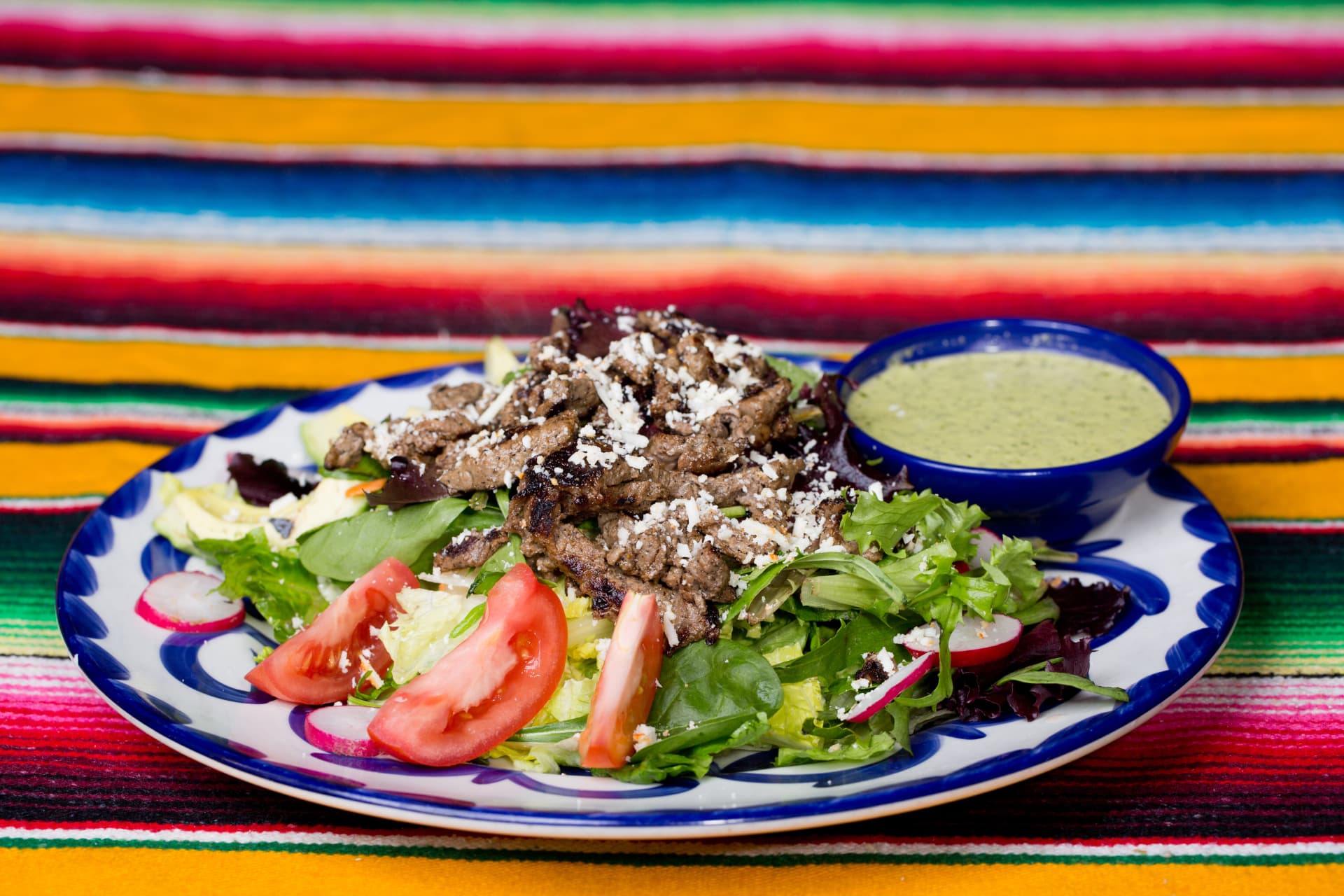 Carne asada salad with mixed greens, tomatoes, radishes, cheese, and cilantro dressing
