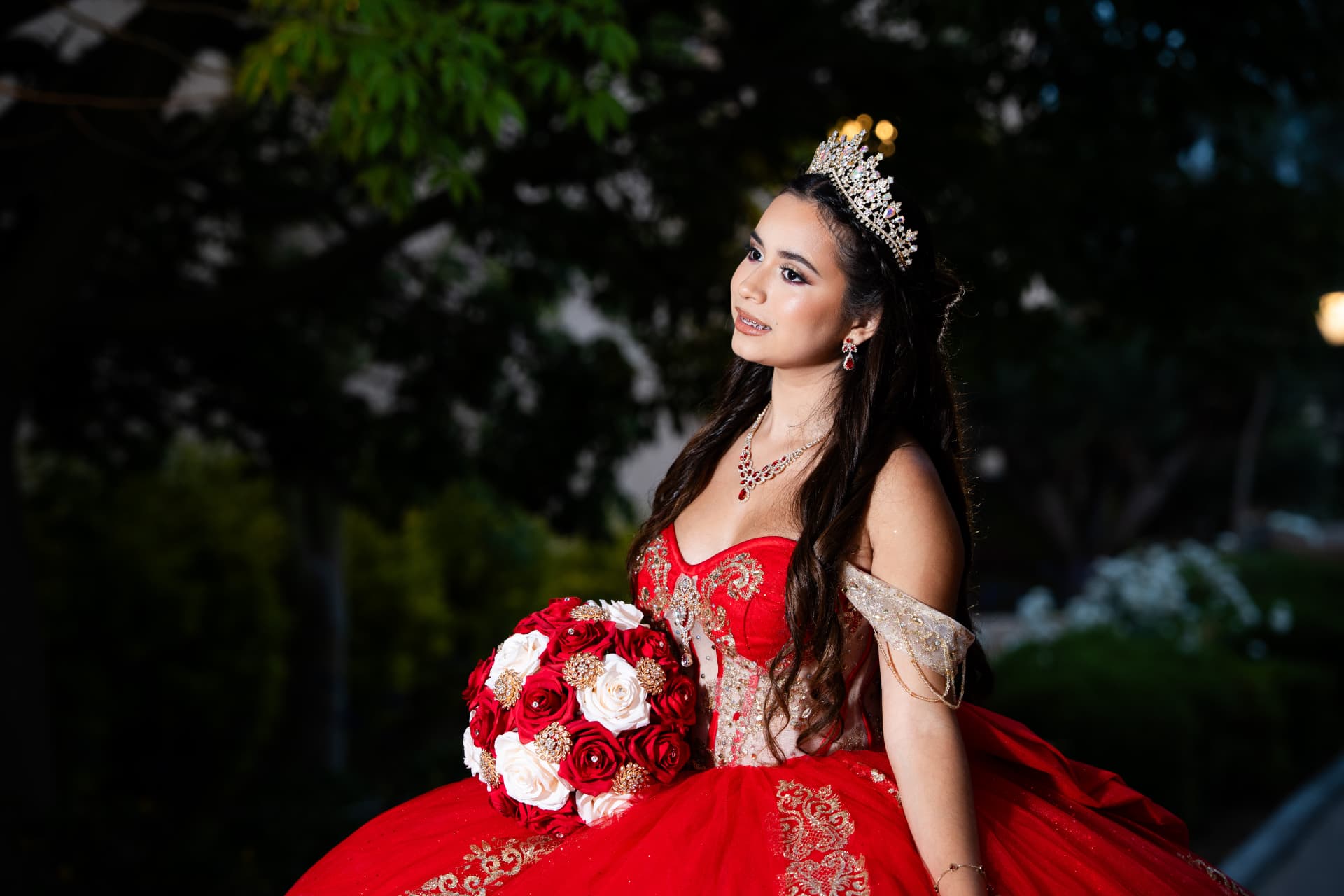 Quinceañera in a red gown with her red and white rose bouquet at night