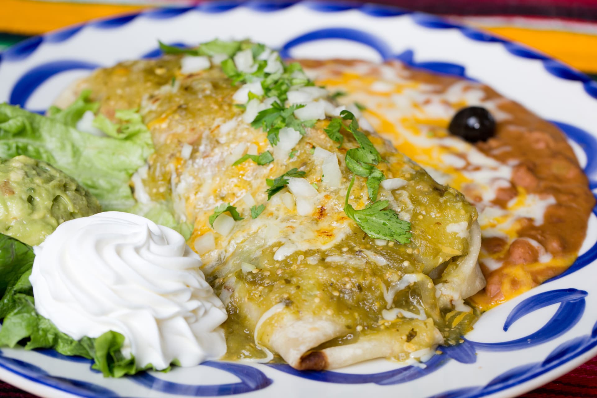 Green enchiladas topped with cheese, onion, and cilantro beside beans and guacamole