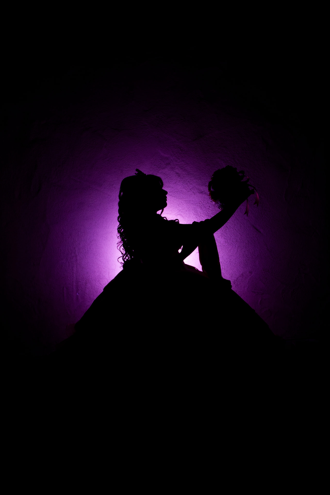 Silhouette of a quinceañera in purple light lifting her bouquet