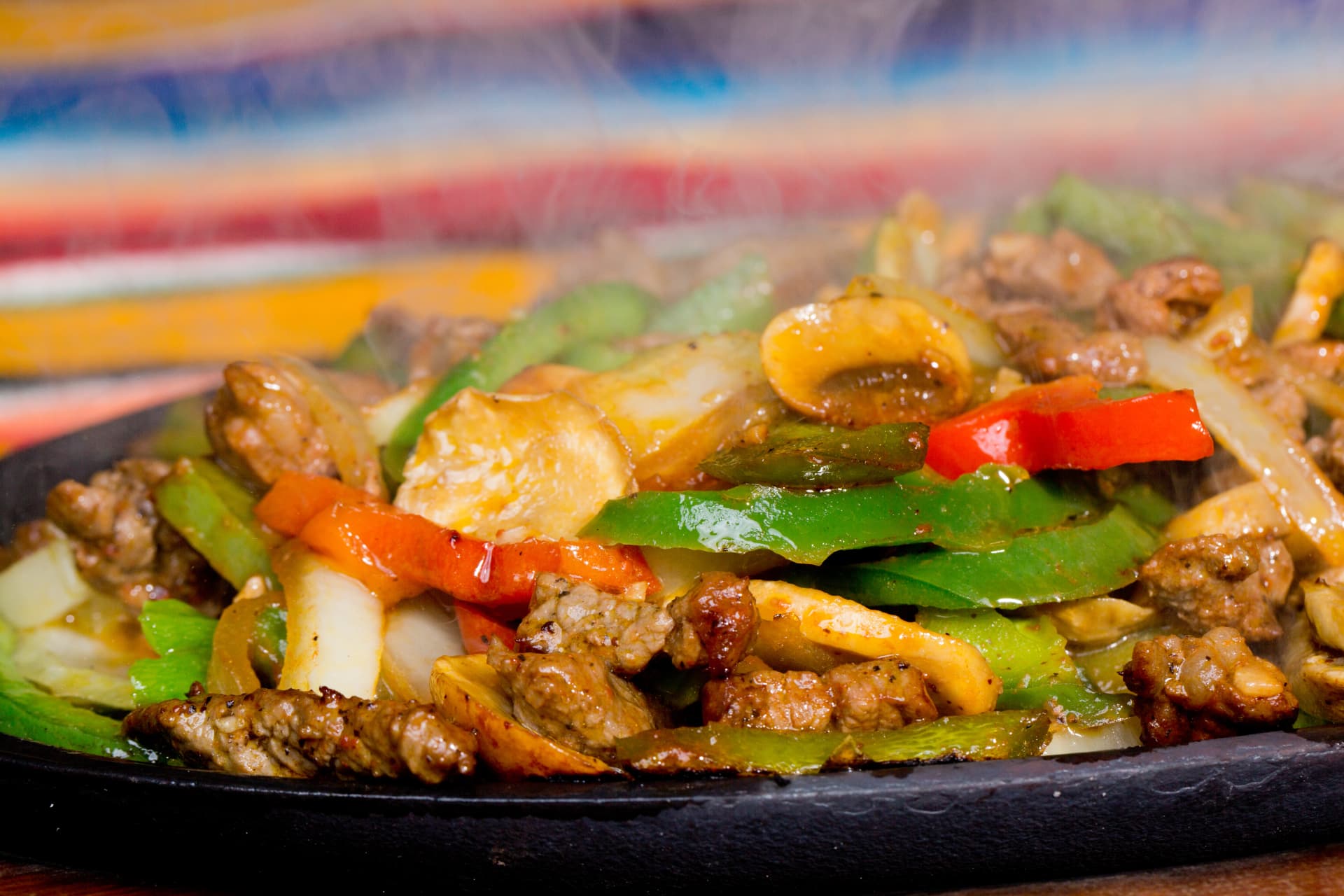 Steaming beef fajitas with mushrooms, peppers, and onions on a sizzling skillet