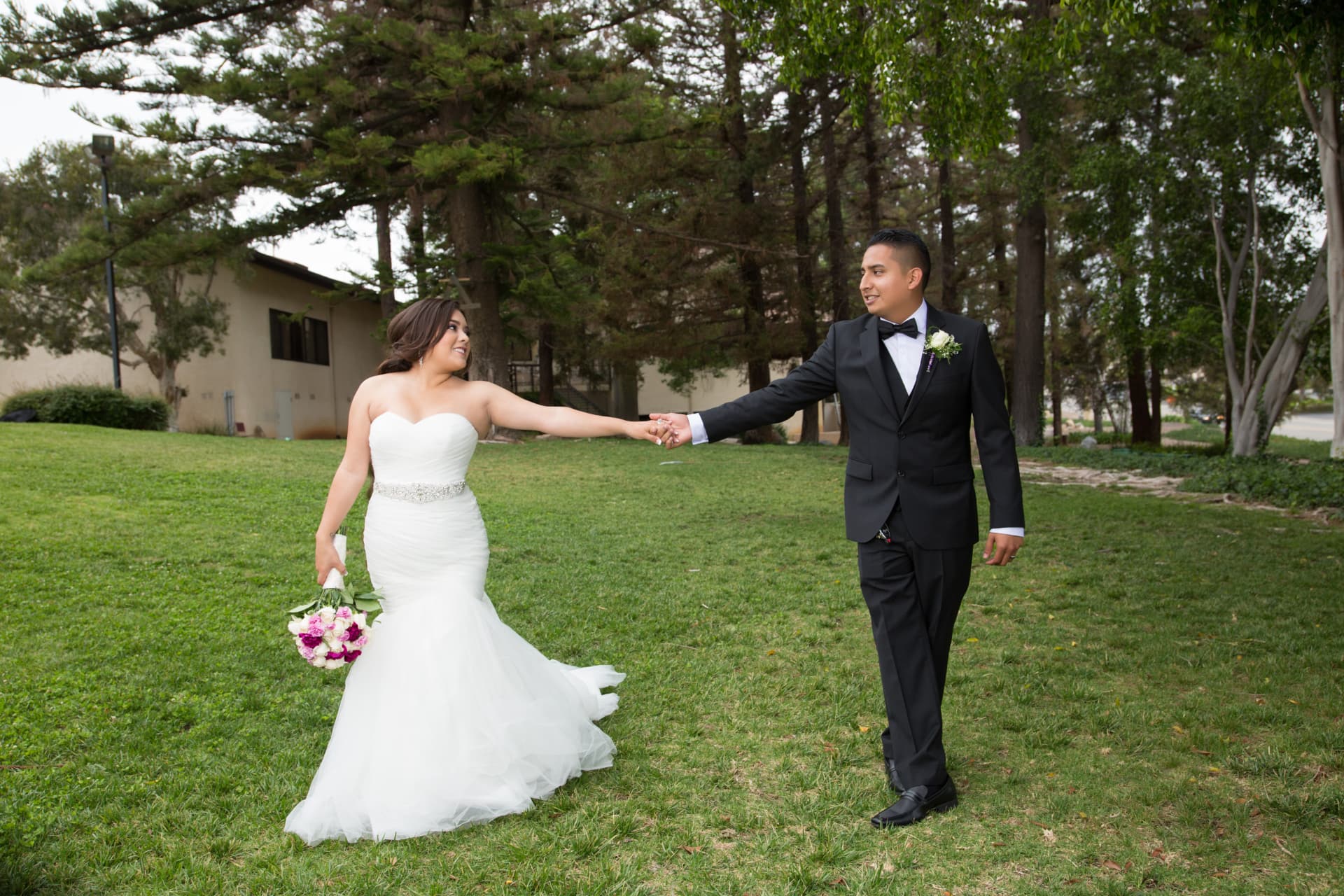 Bride and groom holding hands as they walk together across a green lawn