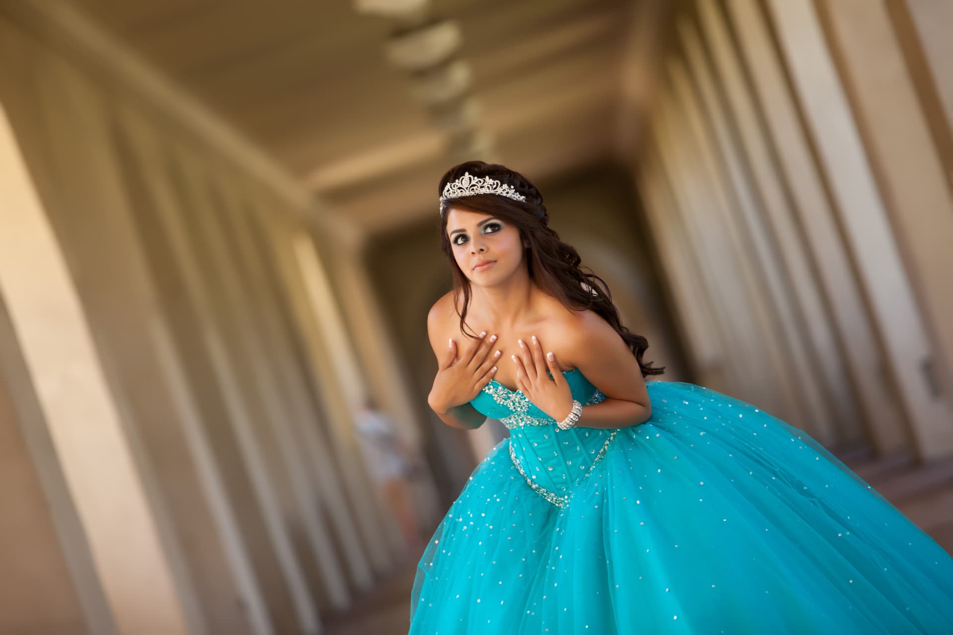 Quinceañera in a turquoise beaded gown smiling in an arched corridor