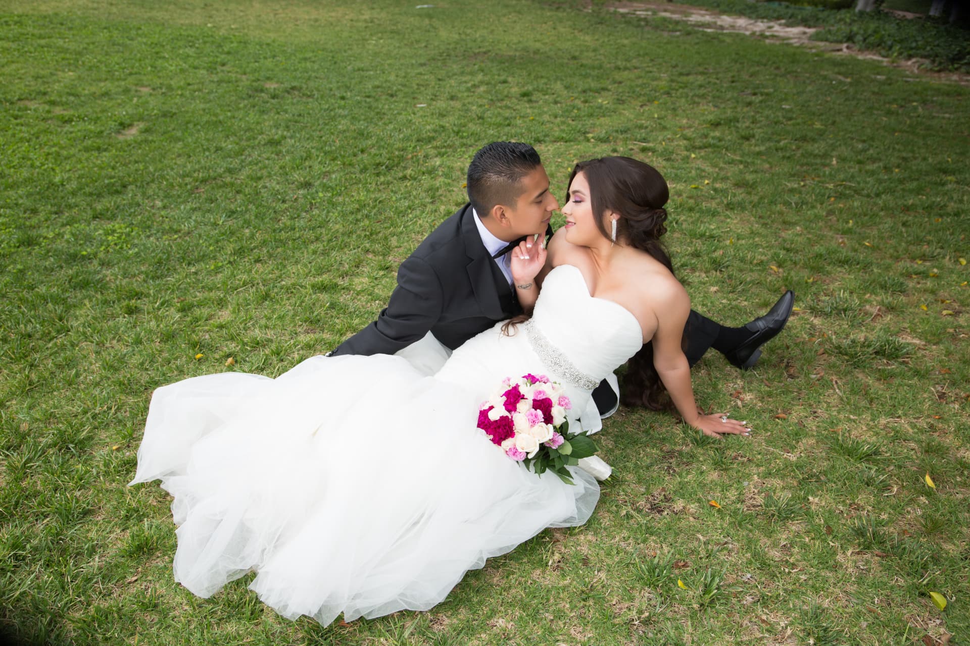 Bride and groom leaning close together as her white gown fans across a green lawn
