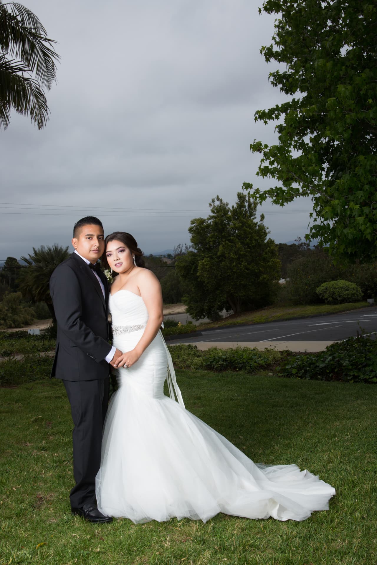 Bride and groom posing together beneath an overcast sky in a garden