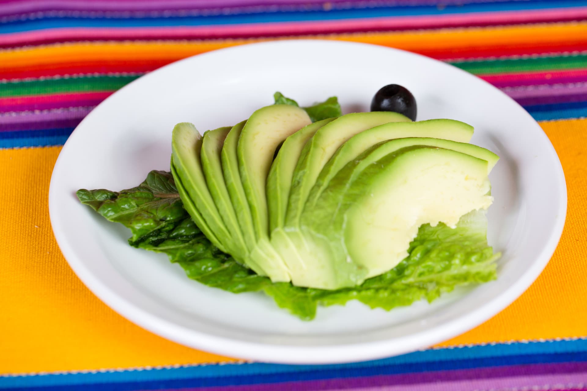 Fresh avocado slices arranged on lettuce over a colorful woven tablecloth